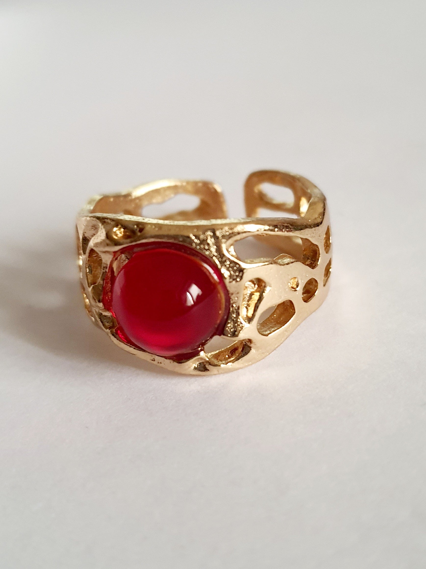 Złoty pierścionek artystyczny z czerwonym kaboszonem, stal nierdzewna, ażurowa forma, rozmiar 16 mm, elegancki i wyrazisty. Rouge Bizu.

