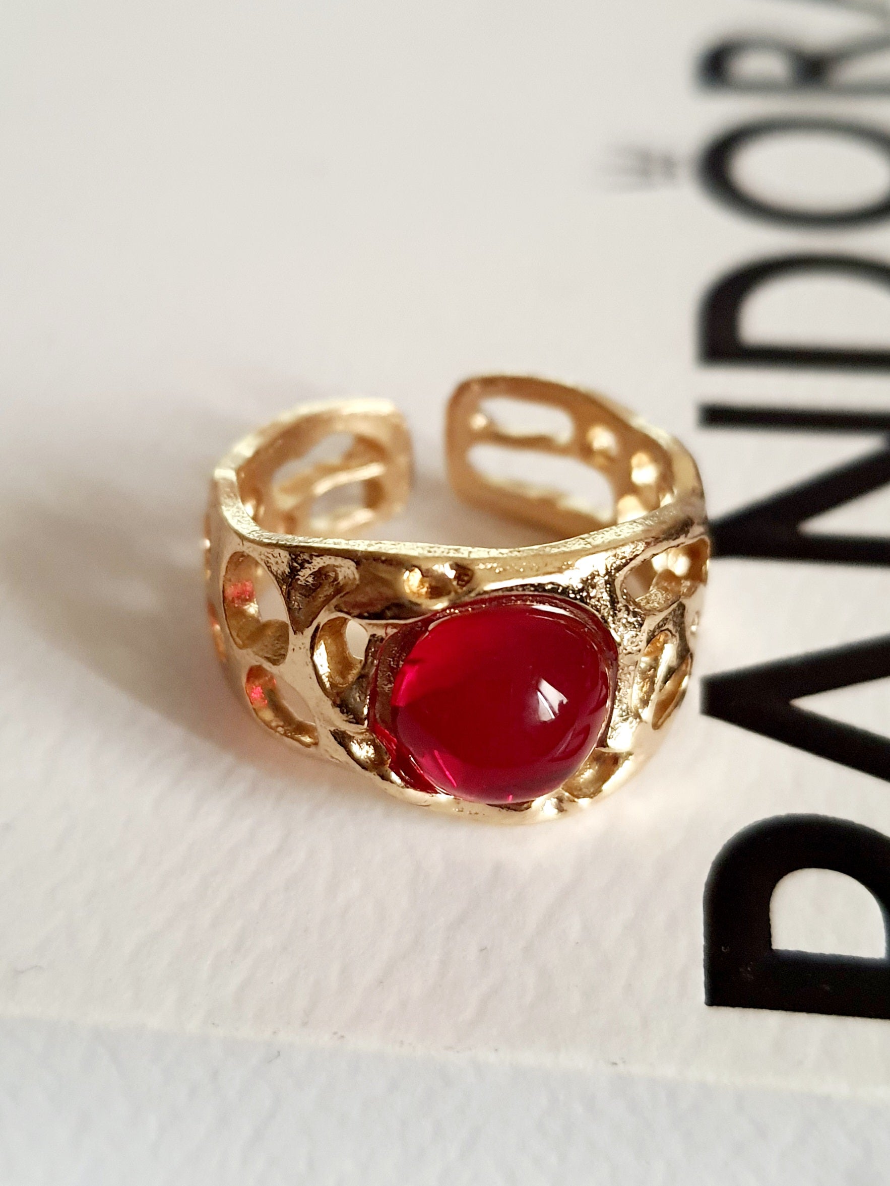 Złoty pierścionek artystyczny z czerwonym kaboszonem, stal nierdzewna, ażurowa forma, rozmiar 16 mm, elegancki i wyrazisty. Rouge Bizu.

