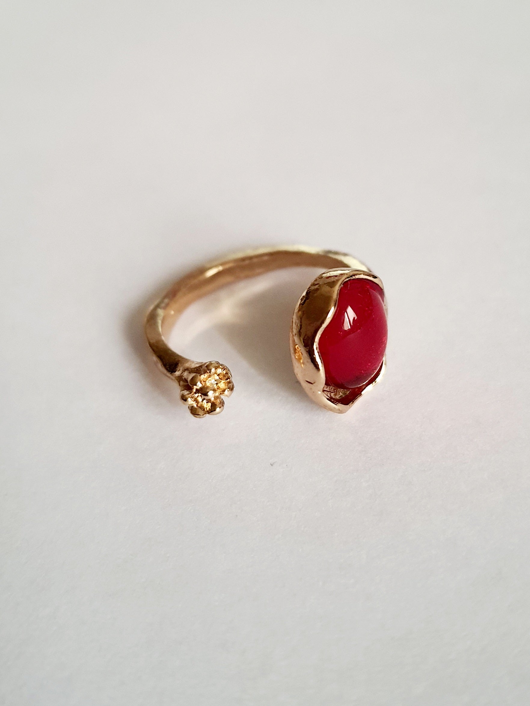 Złoty pierścionek z czerwonym syntetycznym kamieniem i drobnym kwiatowym detalem, romantyczny styl, stal nierdzewna, rozmiar 16 mm. Rouge Bizu.

