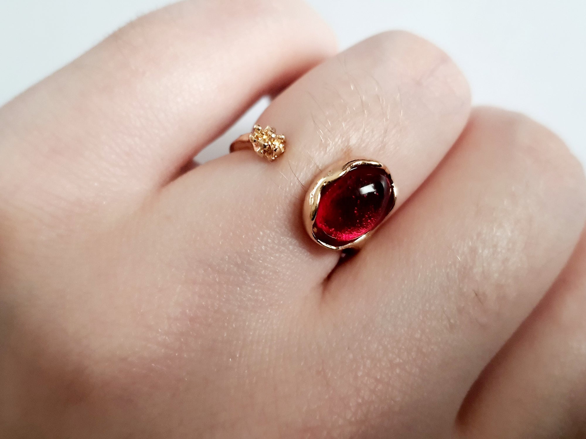 Złoty pierścionek z czerwonym syntetycznym kamieniem i drobnym kwiatowym detalem, romantyczny styl, stal nierdzewna, rozmiar 16 mm. Rouge Bizu.

