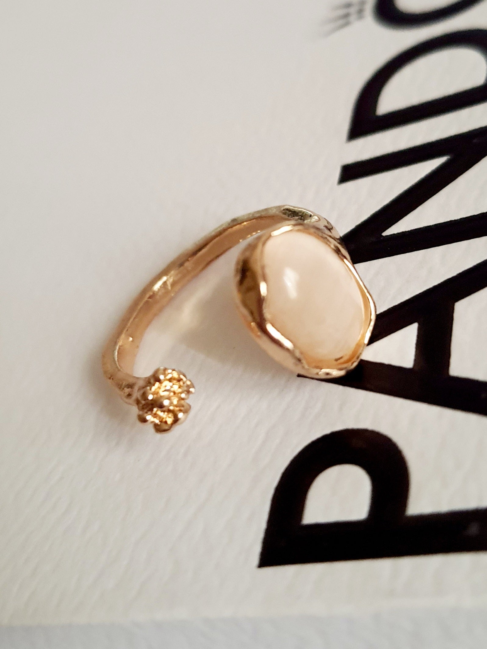 Złoty pierścionek ze stali nierdzewnej z kremowym syntetycznym kamieniem i małym kwiatowym detalem, subtelny styl organiczny, regulowany, rozmiar 15 mm. Rouge Bizu.

