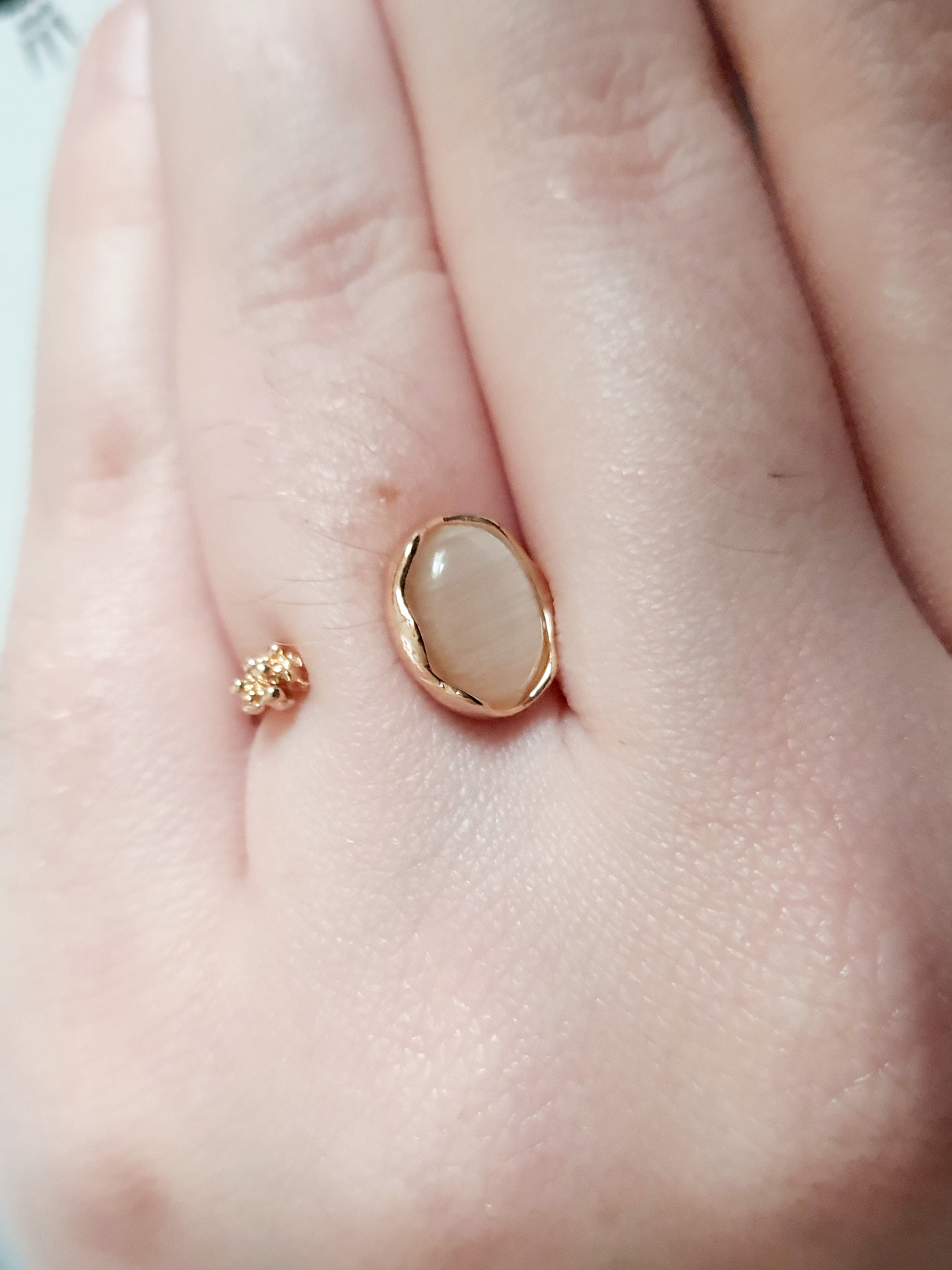 Złoty pierścionek ze stali nierdzewnej z kremowym syntetycznym kamieniem i małym kwiatowym detalem, subtelny styl organiczny, regulowany, rozmiar 15 mm. Rouge Bizu.

