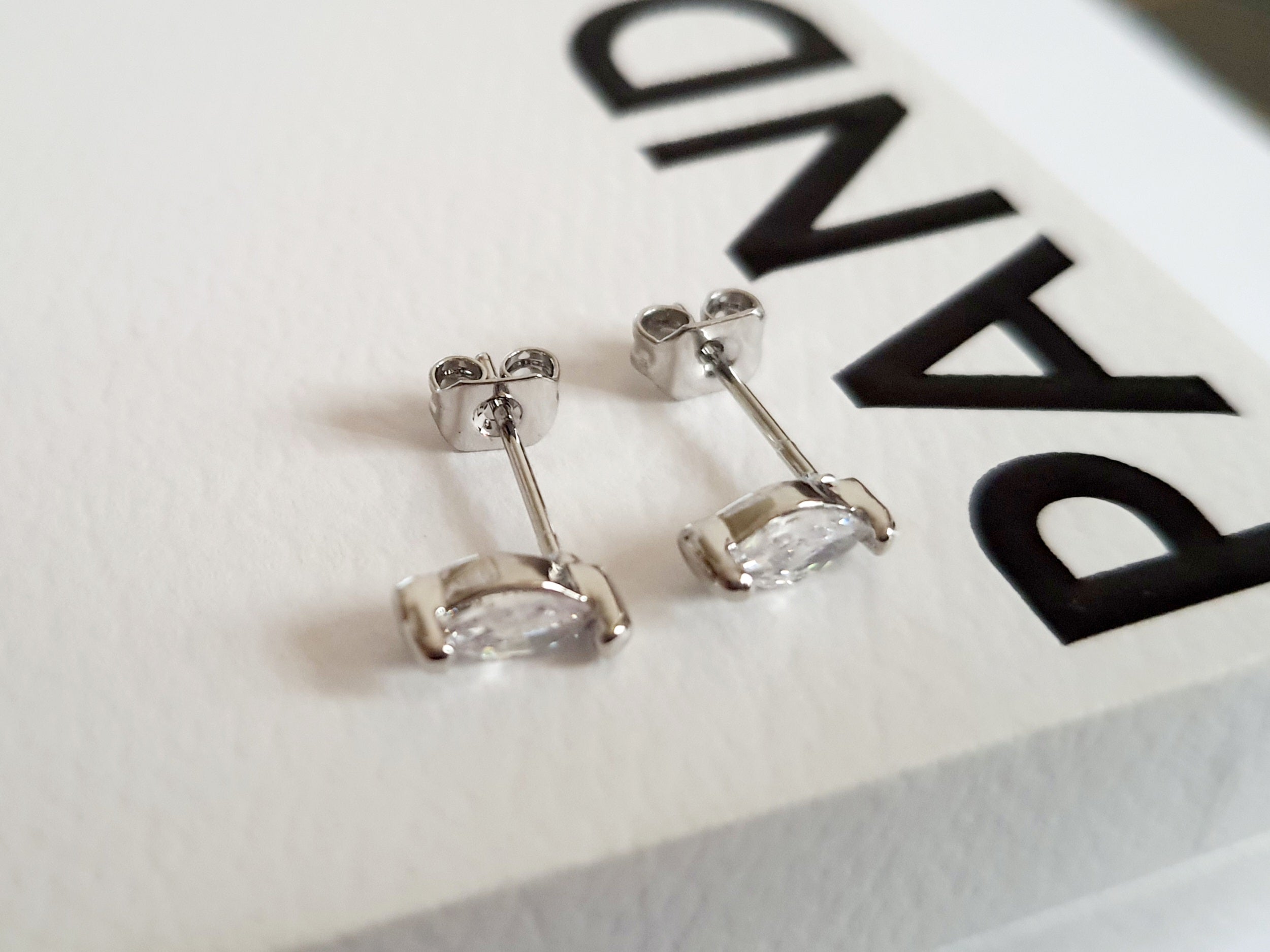 Srebrne kolczyki wkrętki ze stali nierdzewnej z przezroczystym kryształem w szlifie markiza, minimalistyczny styl, długość 1 cm, delikatne i eleganckie. Rouge Bizu.

