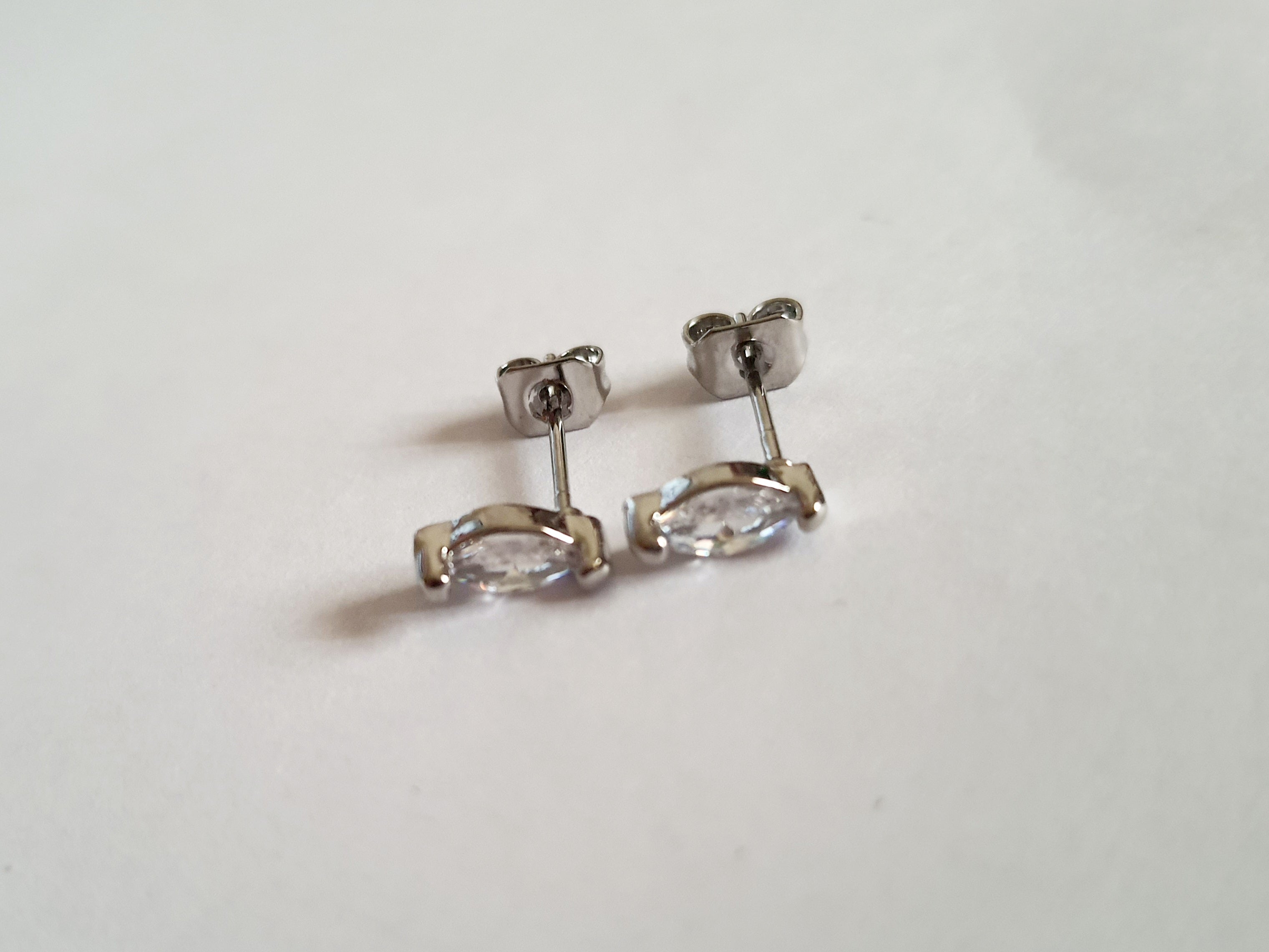 Srebrne kolczyki wkrętki ze stali nierdzewnej z przezroczystym kryształem w szlifie markiza, minimalistyczny styl, długość 1 cm, delikatne i eleganckie. Rouge Bizu.

