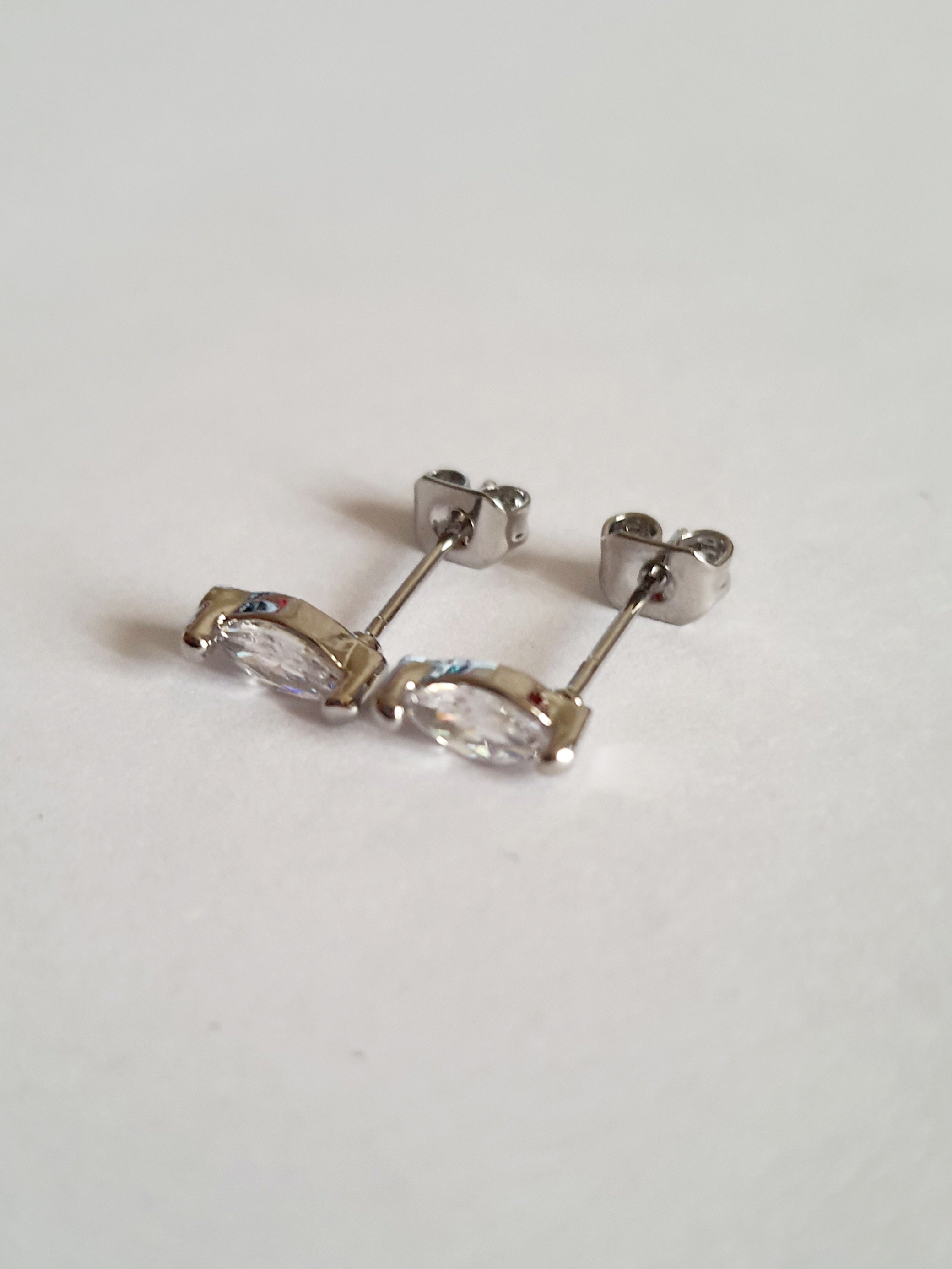 Srebrne kolczyki wkrętki ze stali nierdzewnej z przezroczystym kryształem w szlifie markiza, minimalistyczny styl, długość 1 cm, delikatne i eleganckie. Rouge Bizu.

