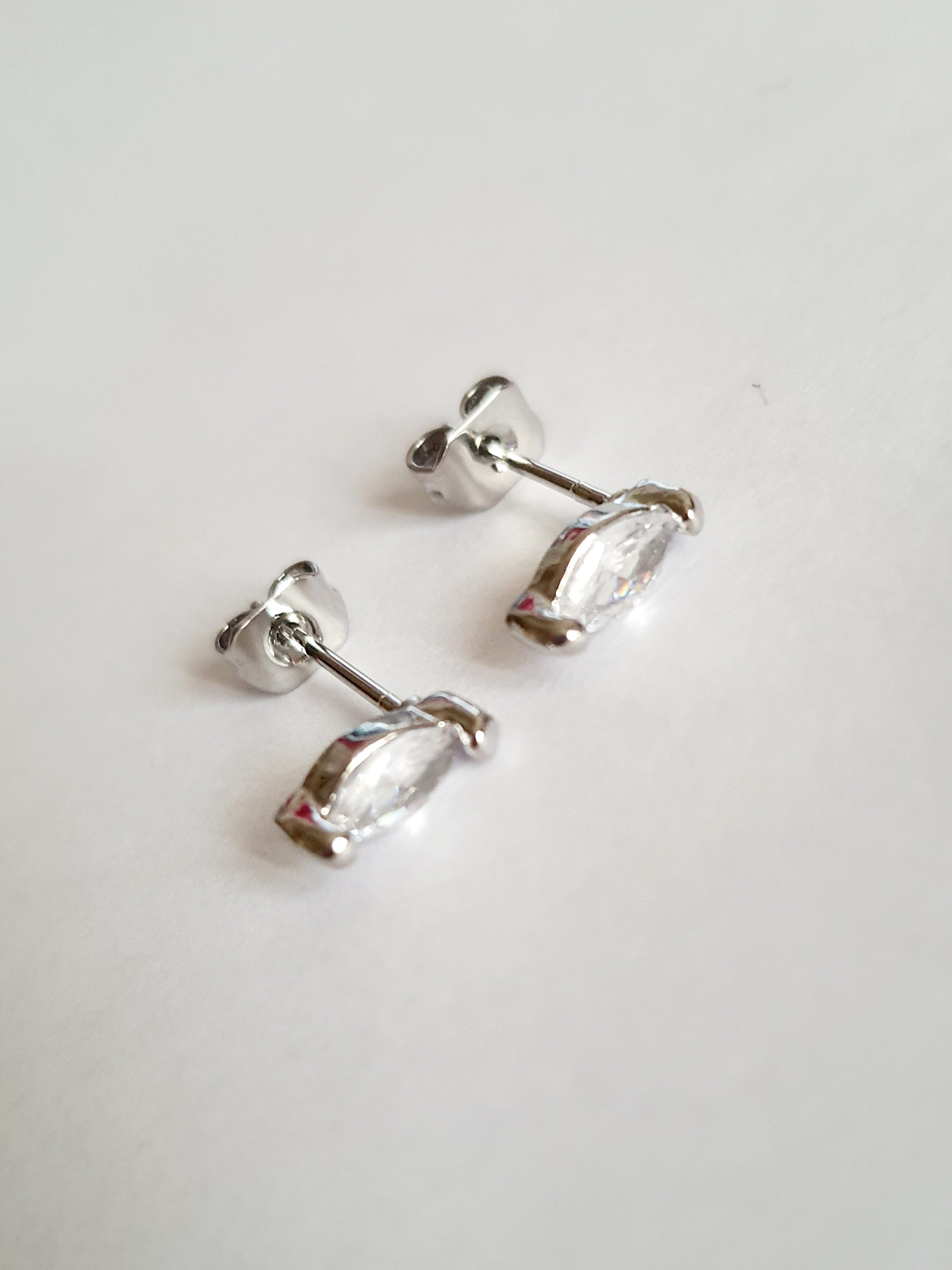 Srebrne kolczyki wkrętki ze stali nierdzewnej z przezroczystym kryształem w szlifie markiza, minimalistyczny styl, długość 1 cm, delikatne i eleganckie. Rouge Bizu.

