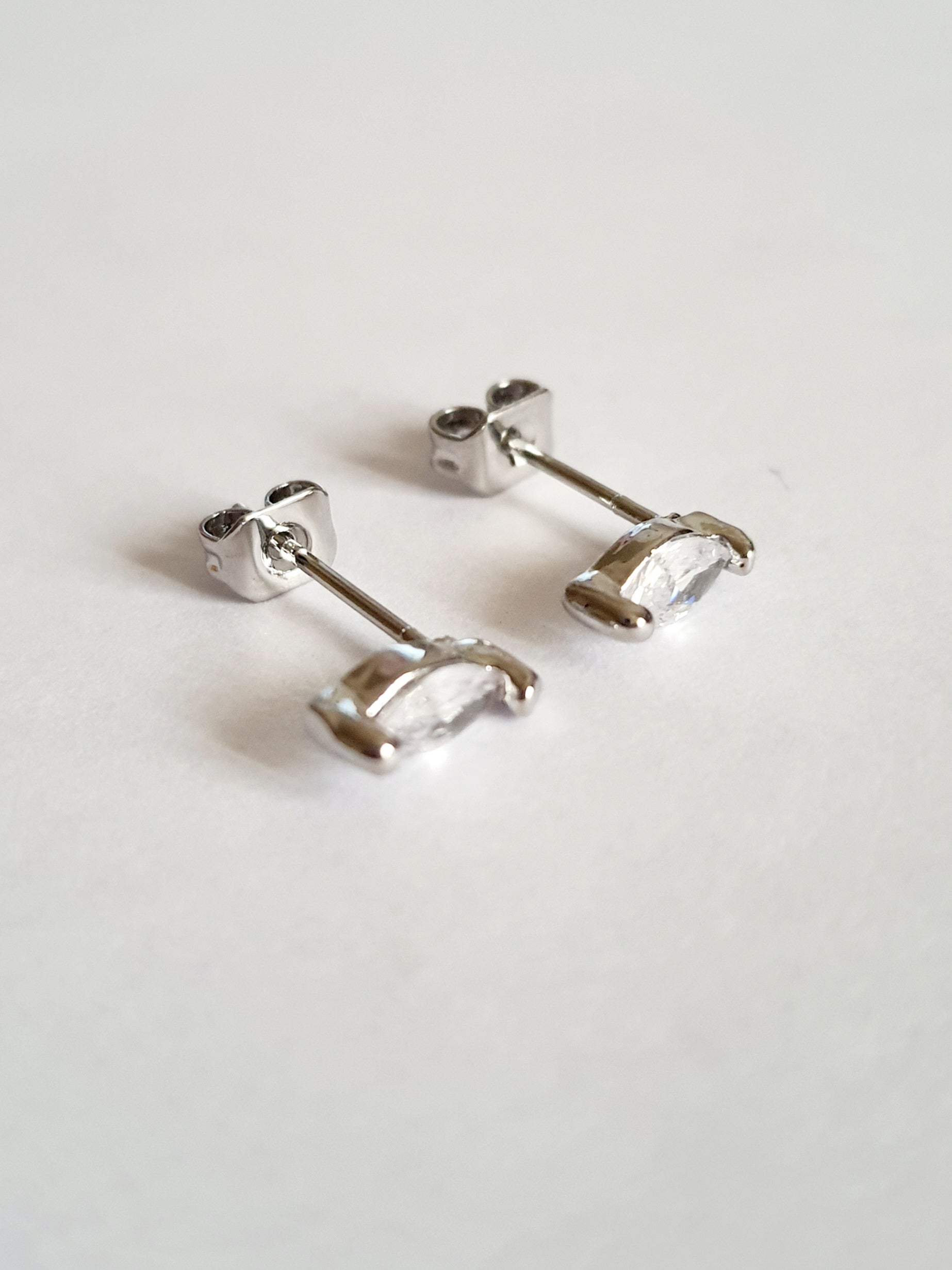 Srebrne kolczyki wkrętki ze stali nierdzewnej z przezroczystym kryształem w szlifie markiza, minimalistyczny styl, długość 1 cm, delikatne i eleganckie. Rouge Bizu.

