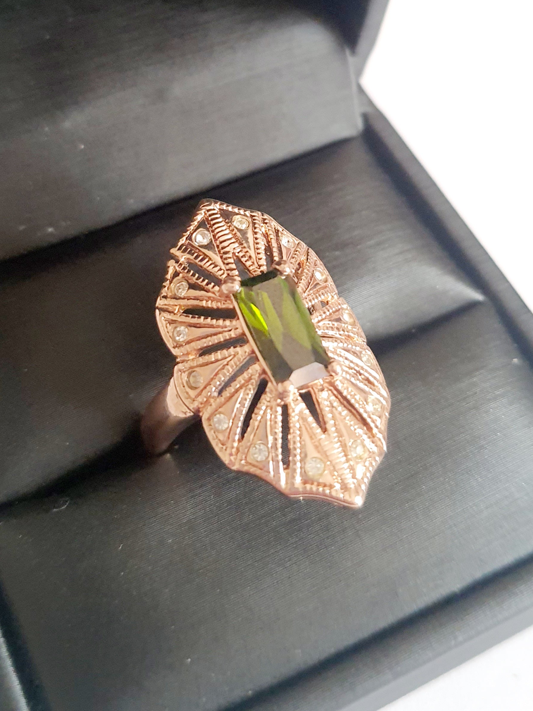 Pierścionek z podłużnym szmaragdowym kamieniem w stylu glamour vintage, oprawiony w wachlarz różowozłotych detali z drobnymi cyrkoniami. Rozmiar 20 mm. Elegancki, kobiecy, wykonany ze stali chirurgicznej. Rouge Bizu.

