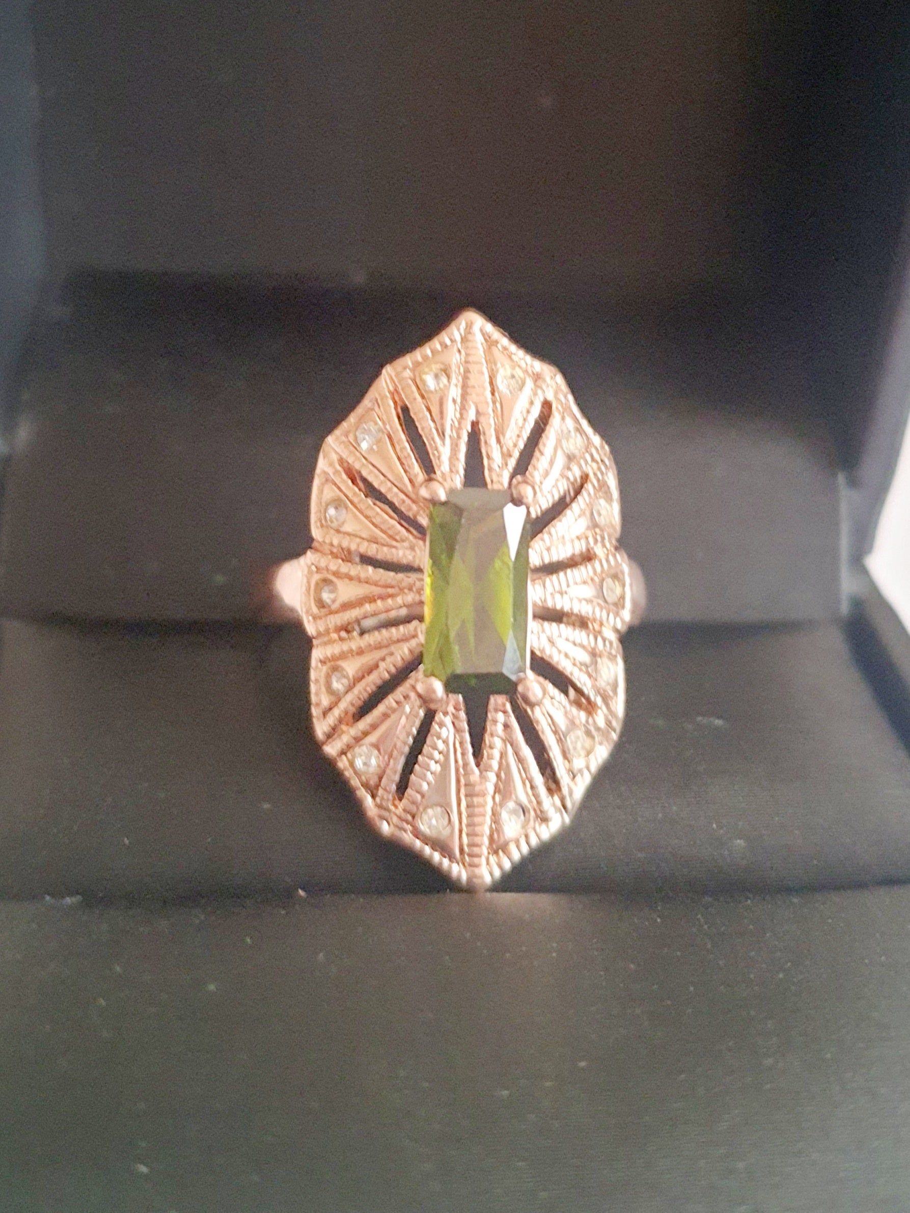 Pierścionek z podłużnym szmaragdowym kamieniem w stylu glamour vintage, oprawiony w wachlarz różowozłotych detali z drobnymi cyrkoniami. Rozmiar 20 mm. Elegancki, kobiecy, wykonany ze stali chirurgicznej. Rouge Bizu.

