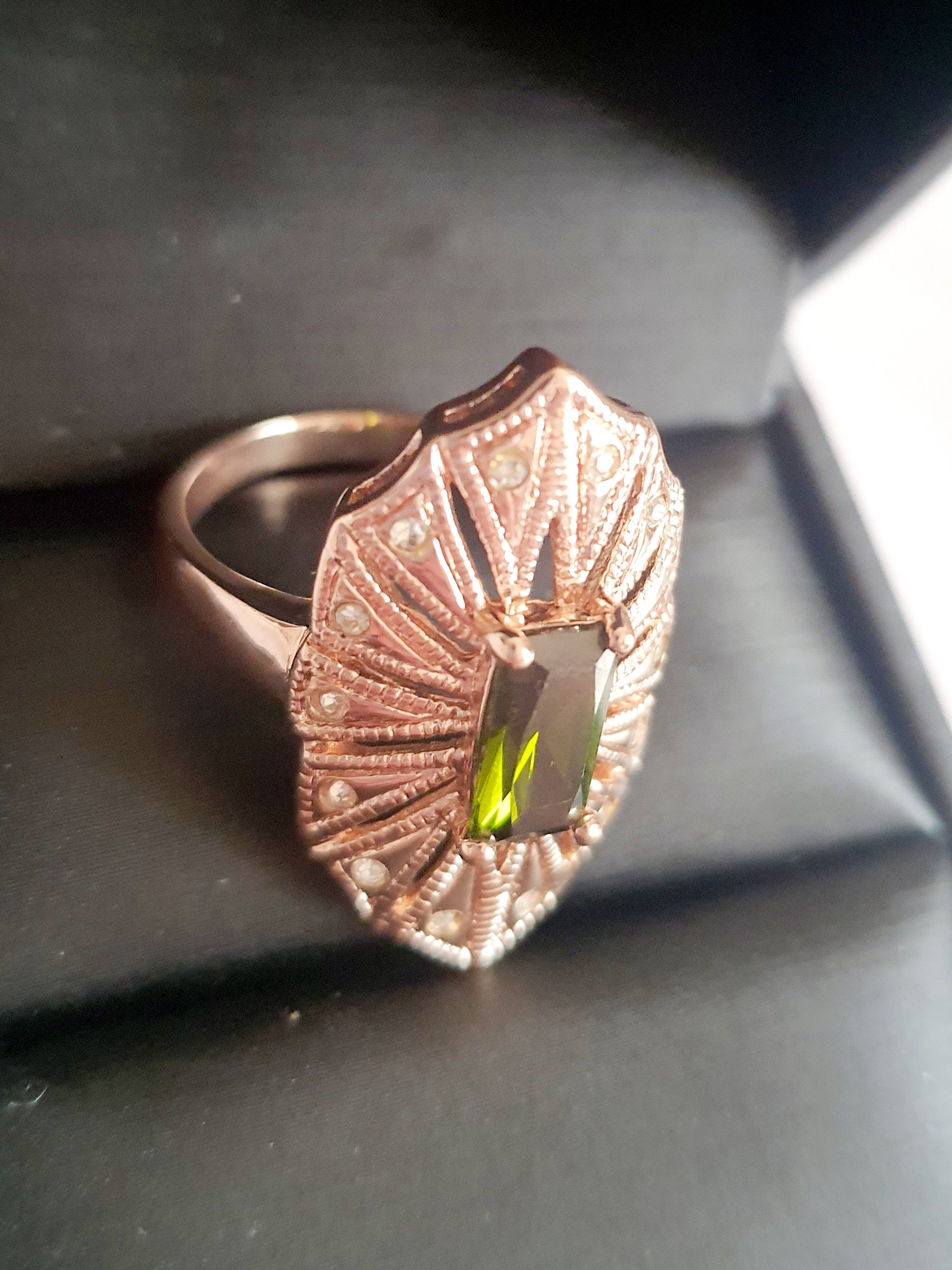 Pierścionek z podłużnym szmaragdowym kamieniem w stylu glamour vintage, oprawiony w wachlarz różowozłotych detali z drobnymi cyrkoniami. Rozmiar 20 mm. Elegancki, kobiecy, wykonany ze stali chirurgicznej. Rouge Bizu.

