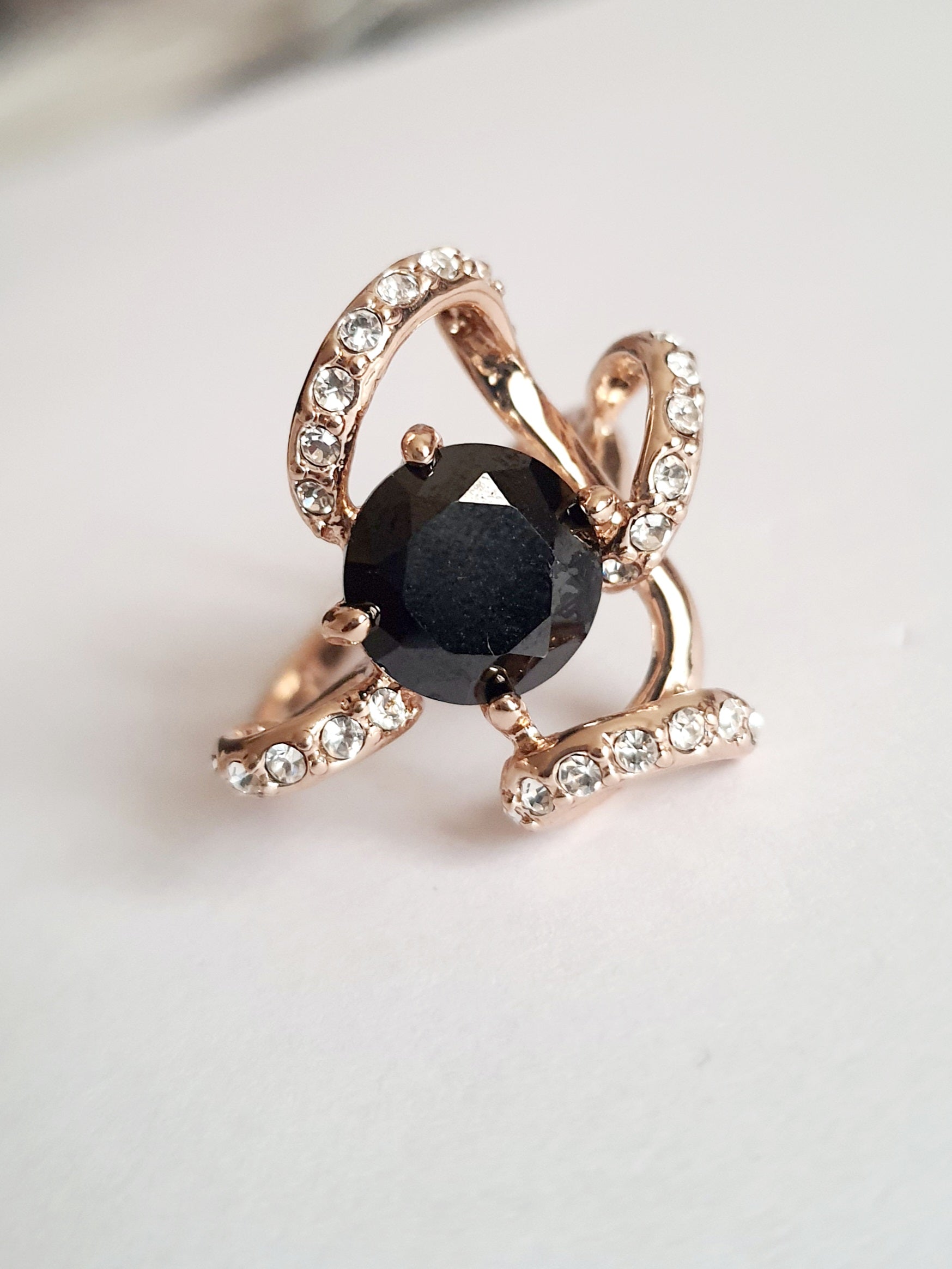 Pierścionek ze złota różowego z dużym czarnym kamieniem w centrum i zdobieniami z drobnych cyrkonii. Styl glamour, rozmiar 18 mm. Elegancki, efektowny, wykonany ze stali chirurgicznej. Rouge Bizu.

