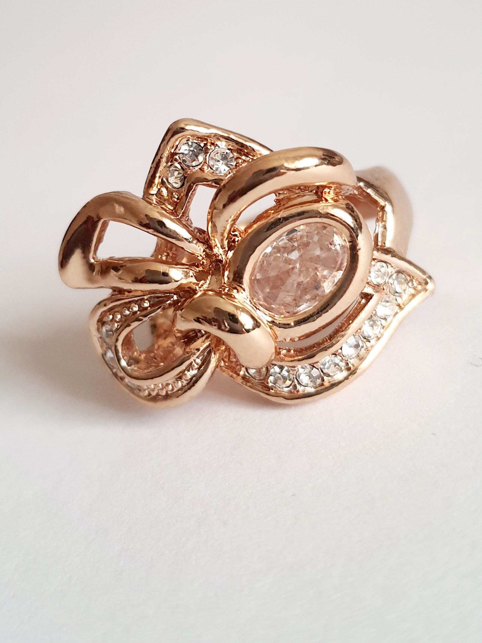 Pierścionek ze stali chirurgicznej w kolorze żółtego złota, z owalnym bezbarwnym kryształem i wijącymi się ramionami zdobionymi cyrkoniami. Styl glamour. Rozmiar 17 mm. Rouge Bizu.

