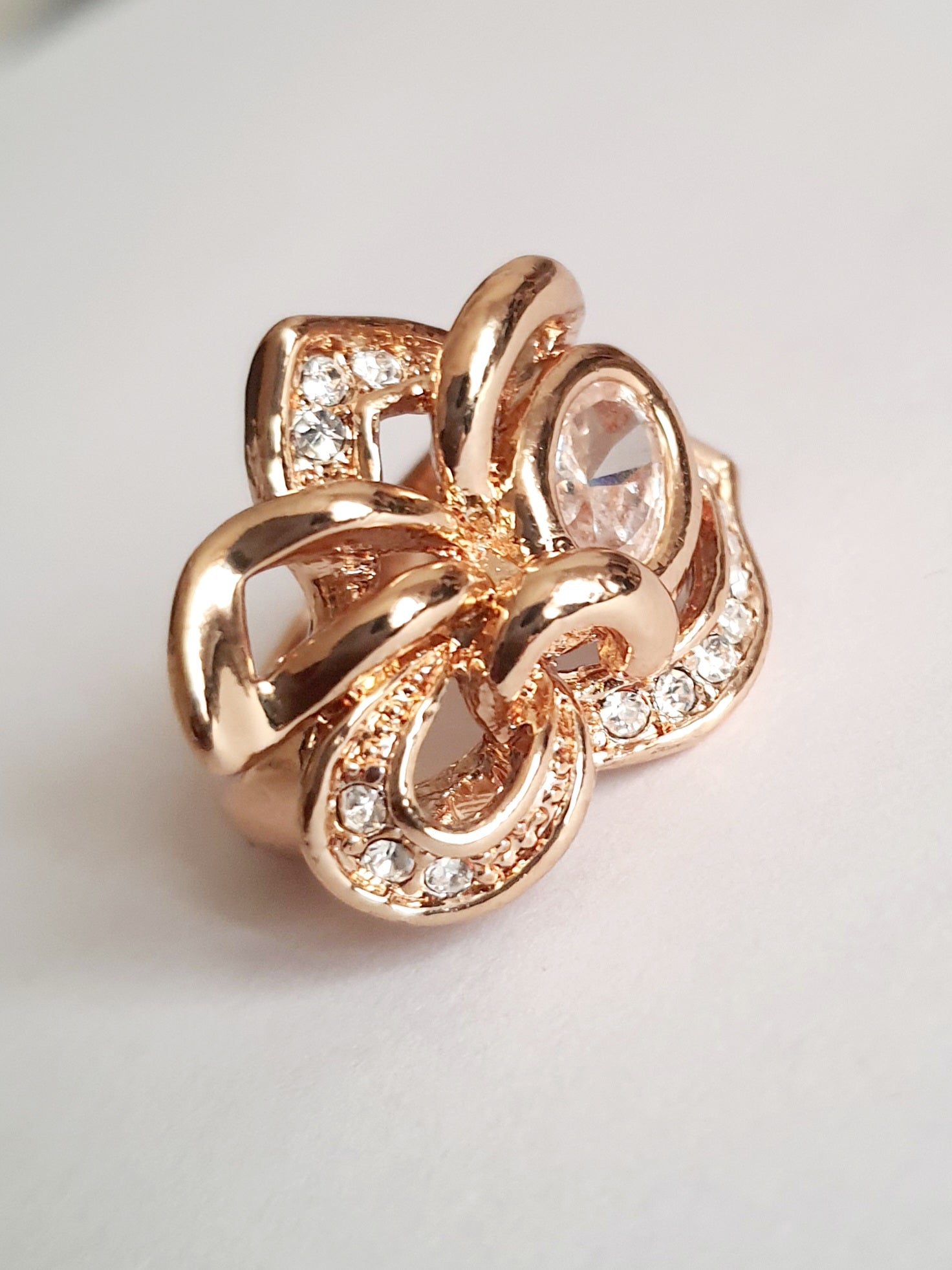 Pierścionek ze stali chirurgicznej w kolorze żółtego złota, z owalnym bezbarwnym kryształem i wijącymi się ramionami zdobionymi cyrkoniami. Styl glamour. Rozmiar 17 mm. Rouge Bizu.

