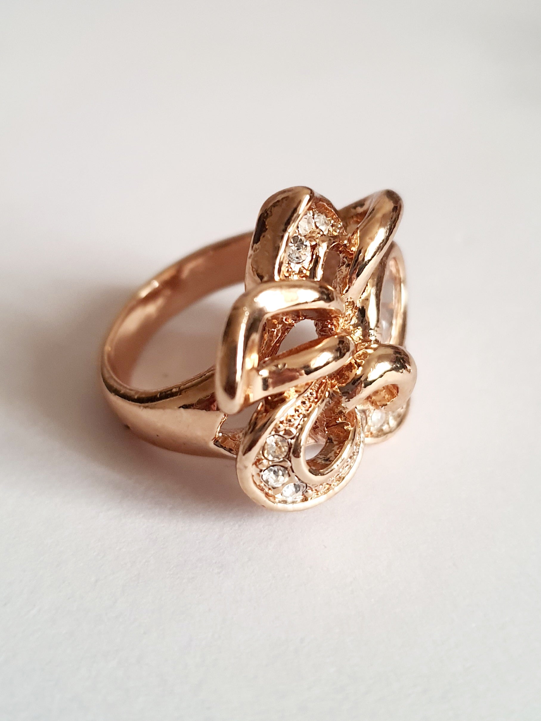 Pierścionek ze stali chirurgicznej w kolorze żółtego złota, z owalnym bezbarwnym kryształem i wijącymi się ramionami zdobionymi cyrkoniami. Styl glamour. Rozmiar 17 mm. Rouge Bizu.

