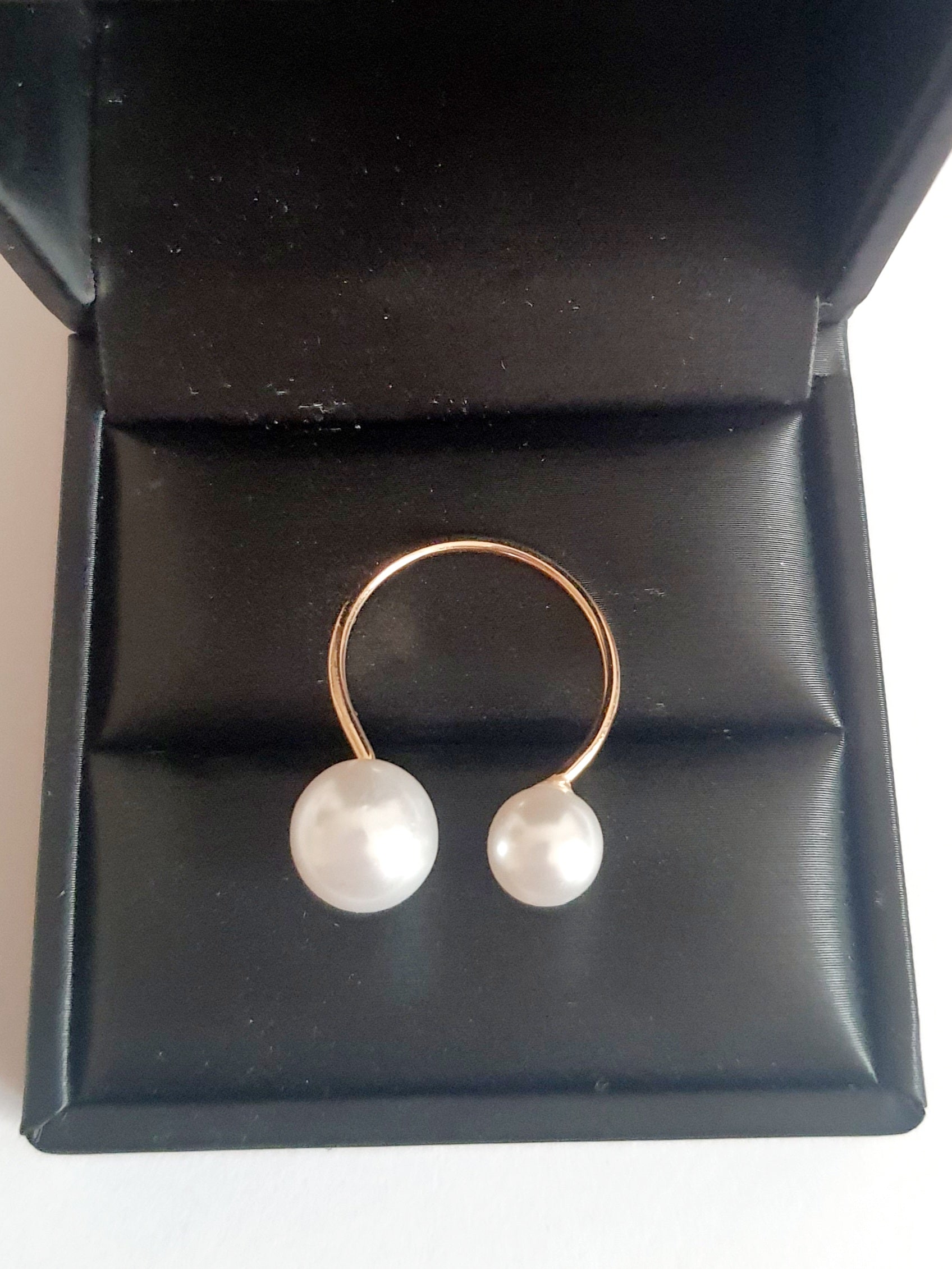 Regulowany pierścionek ze stali chirurgicznej w kolorze żółtego złota, zakończony dwiema białymi syntetycznymi perłami. Minimalistyczny, elegancki design. Rouge Bizu.

