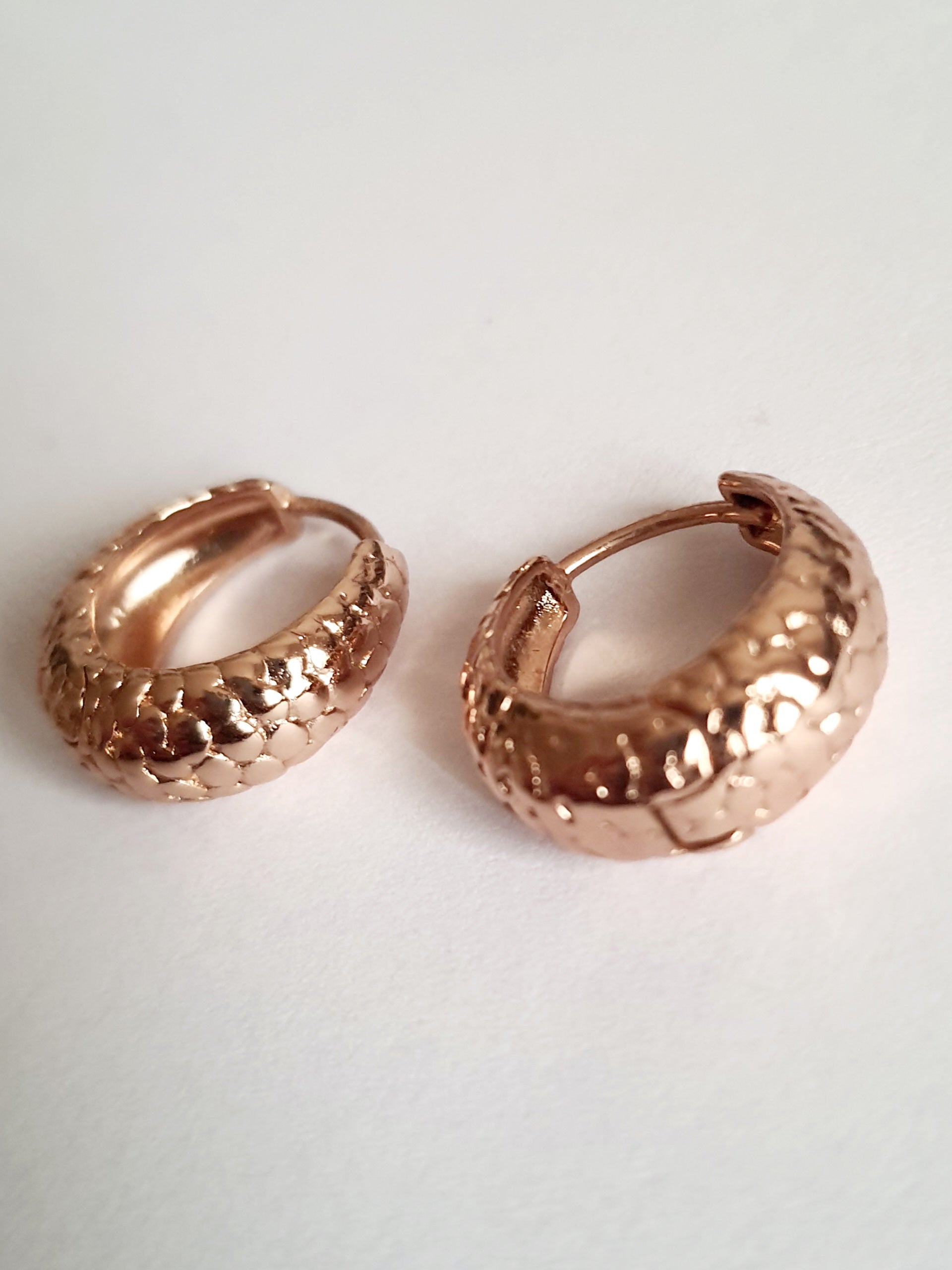 Kolczyki huggie ze stali chirurgicznej w kolorze różowego złota, z młotkowaną fakturą, średnica 1,2 cm. Klasyczny styl z fakturowanym wykończeniem. Rouge Bizu.

