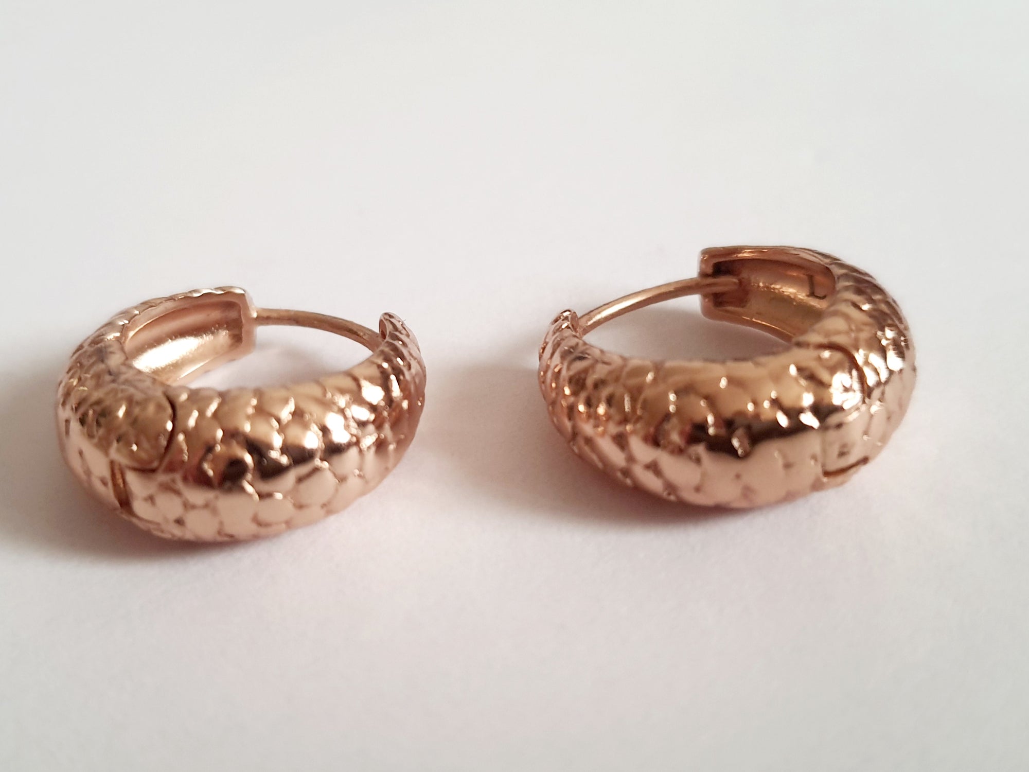 Kolczyki huggie ze stali chirurgicznej w kolorze różowego złota, z młotkowaną fakturą, średnica 1,2 cm. Klasyczny styl z fakturowanym wykończeniem. Rouge Bizu.

