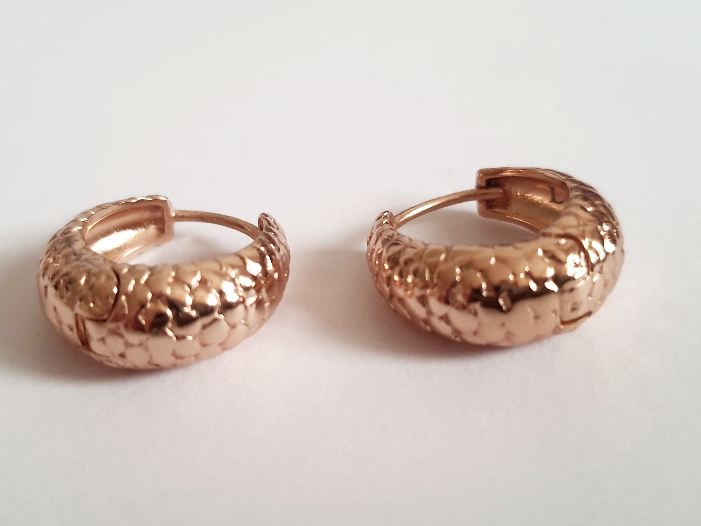 Kolczyki huggie ze stali chirurgicznej w kolorze różowego złota, z młotkowaną fakturą, średnica 1,2 cm. Klasyczny styl z fakturowanym wykończeniem. Rouge Bizu.

