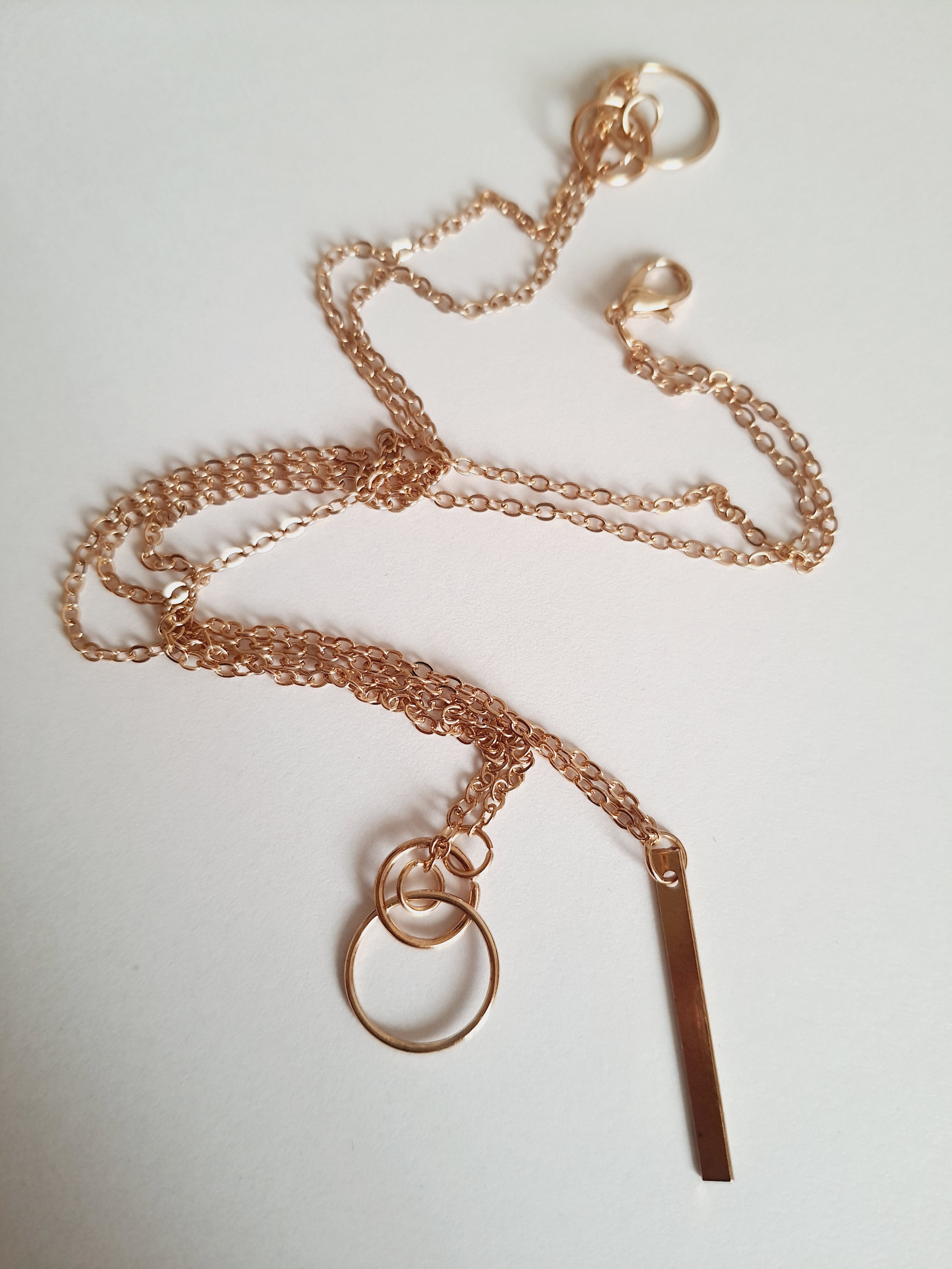 Przewlekany łańcuszek celebrytka ze stali chirurgicznej w kolorze żółtego złota, z dwiema obręczami i prostą podłużną zawieszką. Długość maksymalna 55 cm. Minimalistyczny styl. Rouge Bizu.

