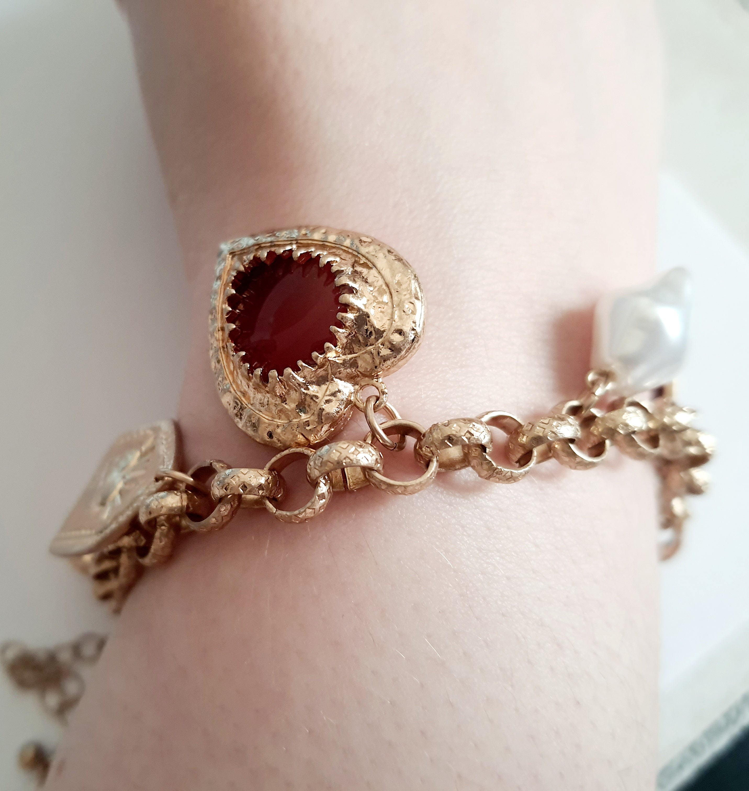 Złota bransoletka w stylu vintage z charmsami: serca, symbole sakralne, perłowe zawieszki. Stal chirurgiczna, długość regulowana 20–28 cm. Klasyka, romantyzm i mistyczna elegancja. Rouge Bizu.

