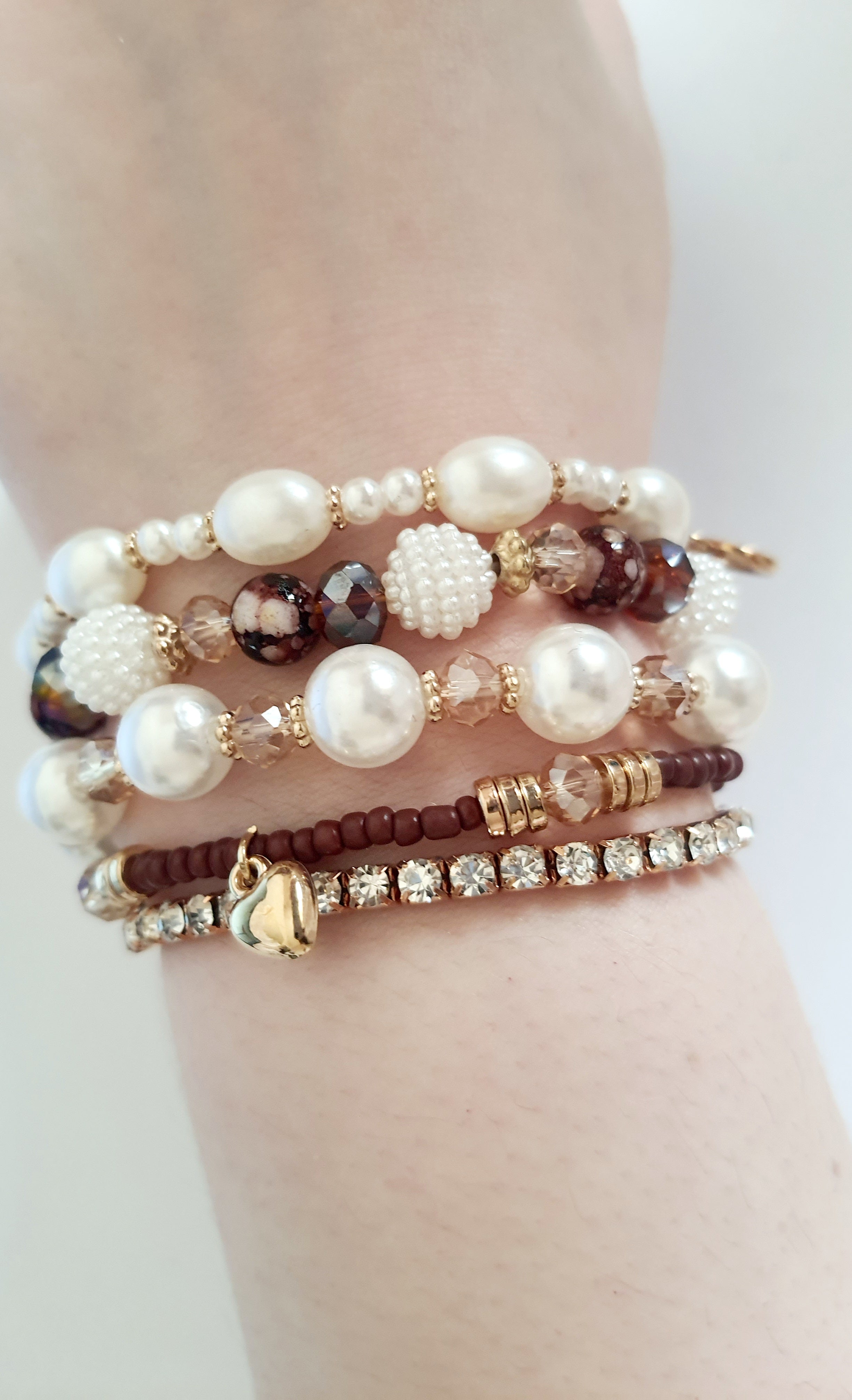 Zestaw pięciu elastycznych bransoletek na gumce z perłami, szkłem, kryształkami i złotymi akcentami. Styl romantyczny i boho. Zawieszka w kształcie serca. Wygodne dopasowanie. Rouge Bizu.

