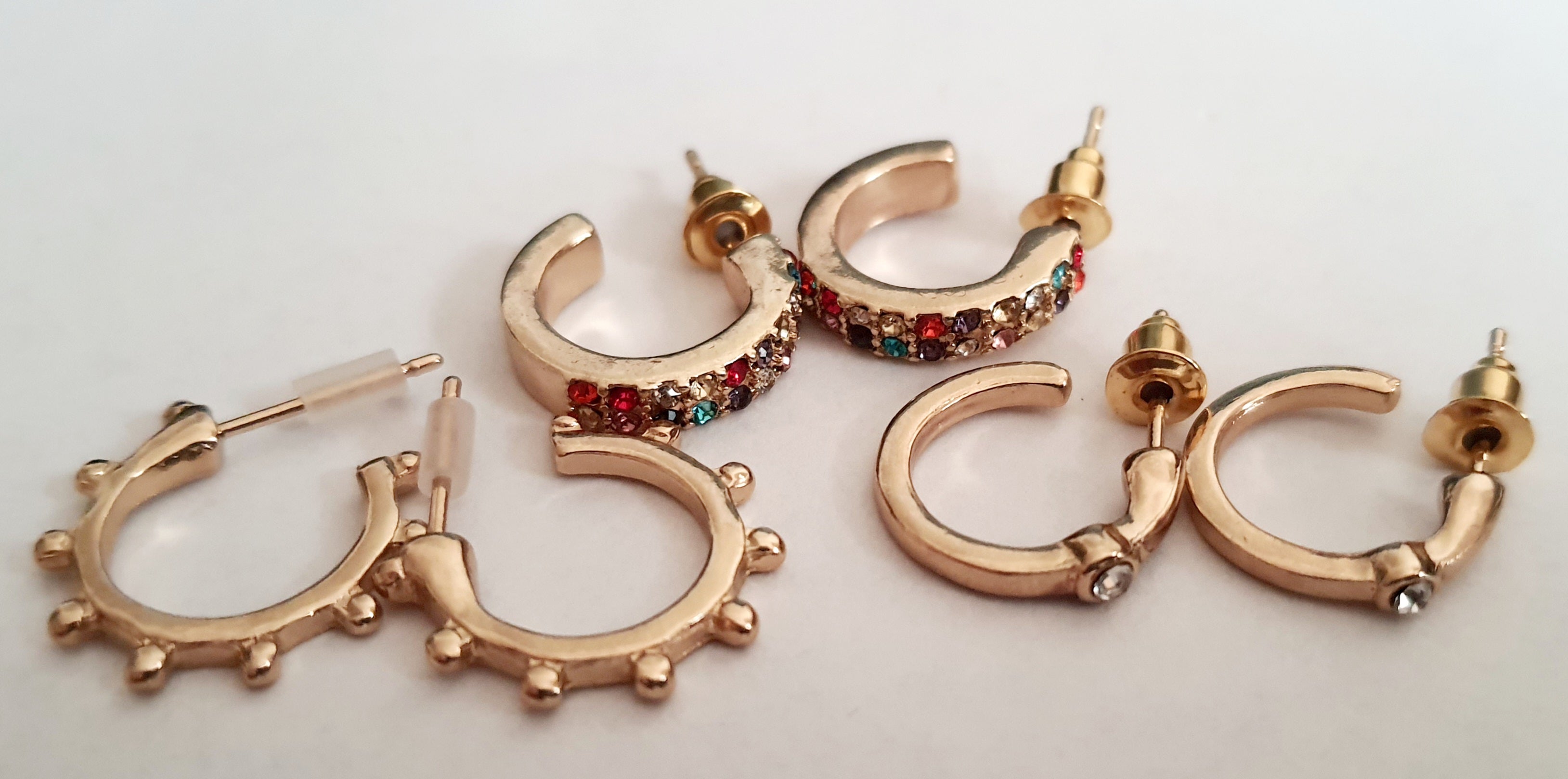 Zestaw 3 par złotych kolczyków typu kółka: kolorowe cyrkonie (1,5 cm), wypustki (1,5 cm), klasyczne z cyrkonią (1 cm). Zapięcie na sztyft. Rouge bizu