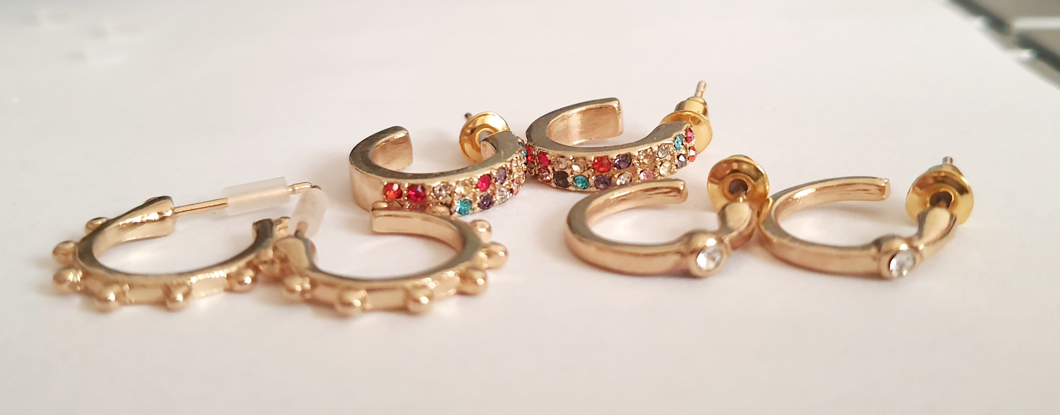 Zestaw 3 par złotych kolczyków typu kółka: kolorowe cyrkonie (1,5 cm), wypustki (1,5 cm), klasyczne z cyrkonią (1 cm). Zapięcie na sztyft. Rouge bizu