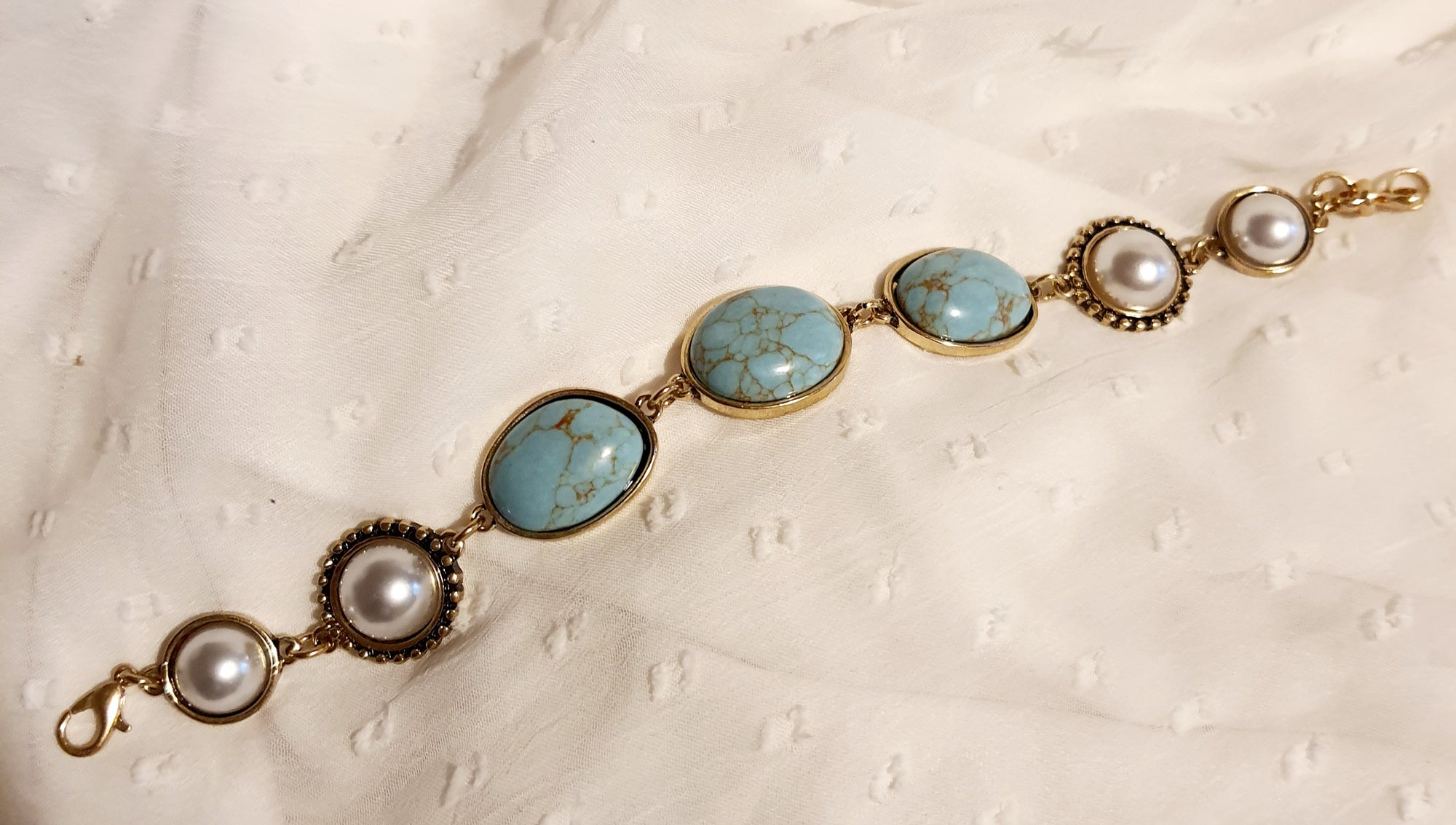 Bransoletka w stylu vintage ze złotą oprawą, ozdobiona turkusowymi kamieniami i perłami. Długość 20 cm. Klasyczna, elegancka forma. Biżuteria ze stali nierdzewnej. Rouge Bizu.

