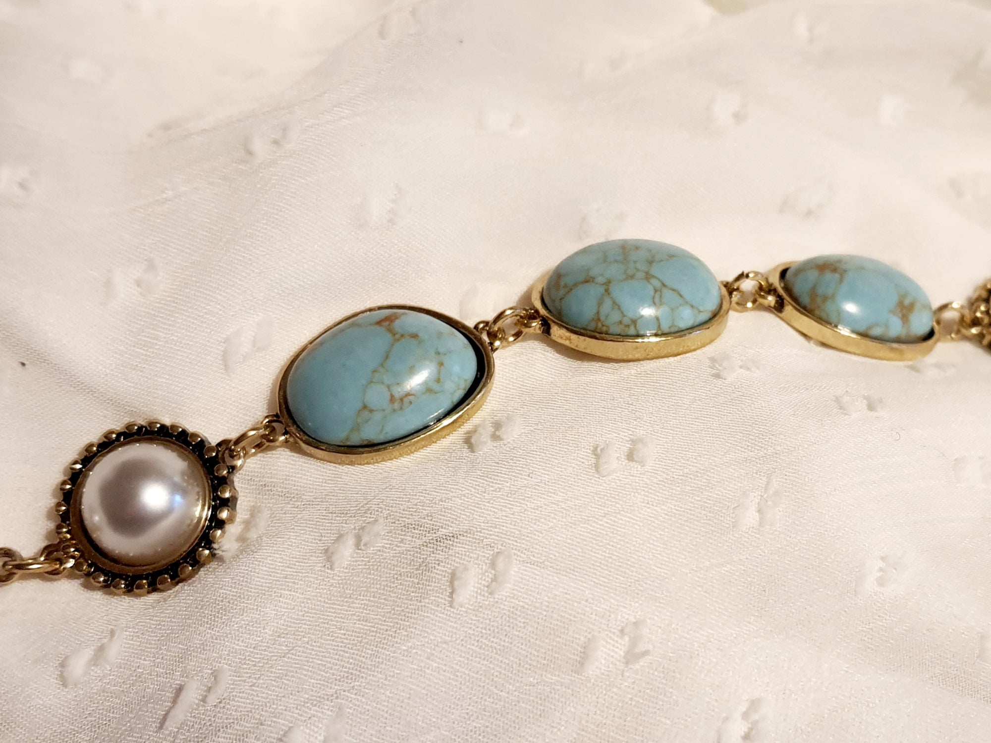 Bransoletka w stylu vintage ze złotą oprawą, ozdobiona turkusowymi kamieniami i perłami. Długość 20 cm. Klasyczna, elegancka forma. Biżuteria ze stali nierdzewnej. Rouge Bizu.

