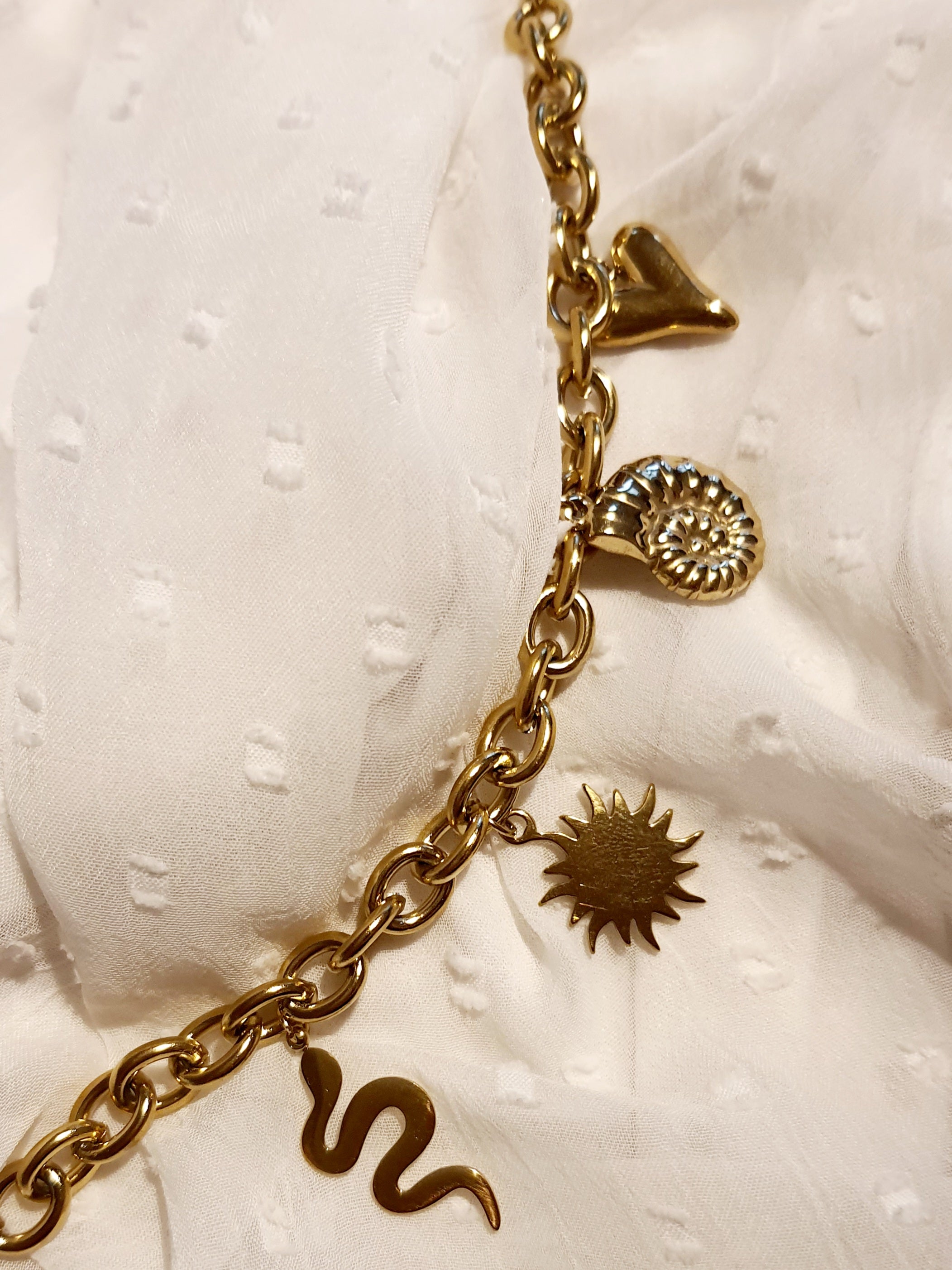 Złota bransoletka w stylu boho z zawieszkami: słońce, muszla, serce, wąż. Regulowana długość 25–30 cm. Talizmaniczna, ze stali nierdzewnej, stal chirurgiczna. Rouge Bizu.

