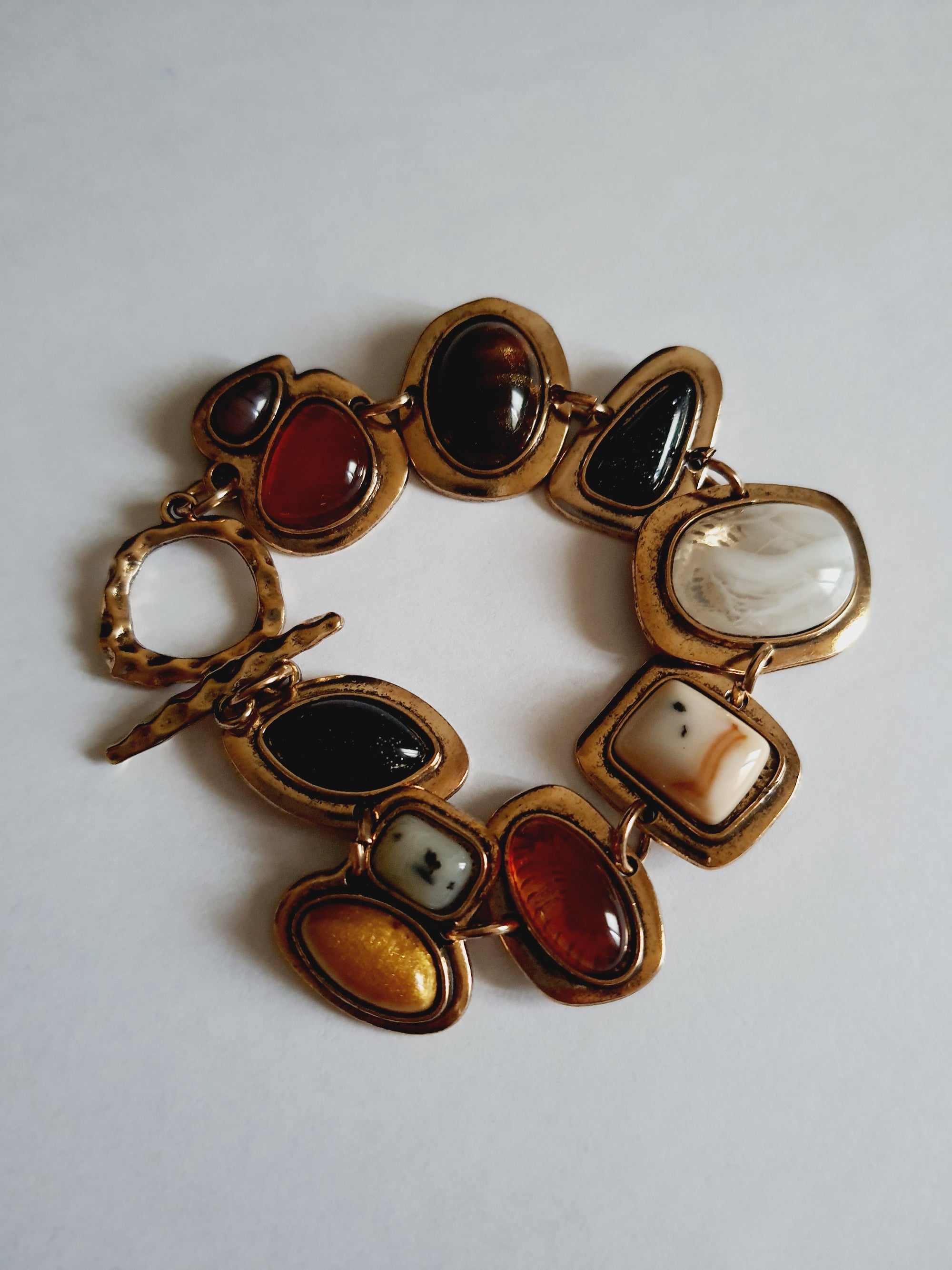 Bransoletka w stylu retro z różnokolorowymi kamieniami – bursztynowymi, czarnymi, marmurkowymi, czerwonymi. Złota oprawa w formie nieregularnych ramek. Długość 20 cm. Stal nierdzewna, stal chirurgiczna. Rouge Bizu.

