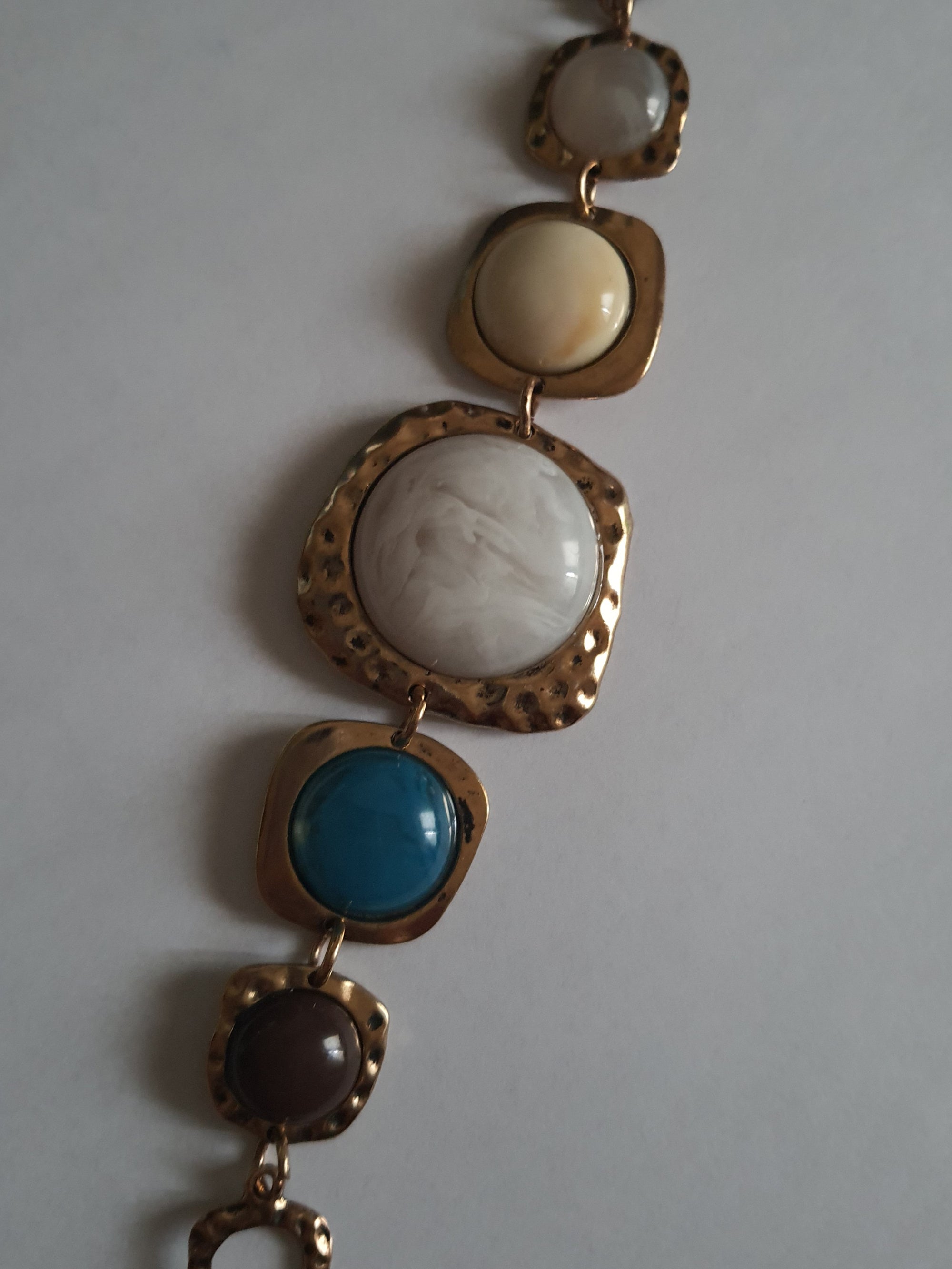 Artystyczna bransoletka damska z medalionami w kolorach marmuru, niebieskiego i brązu w nieregularnych złotych ramkach. Długość 20 cm. Styl boho, wyrazisty design. Stal nierdzewna, stal chirurgiczna. Rouge Bizu.

