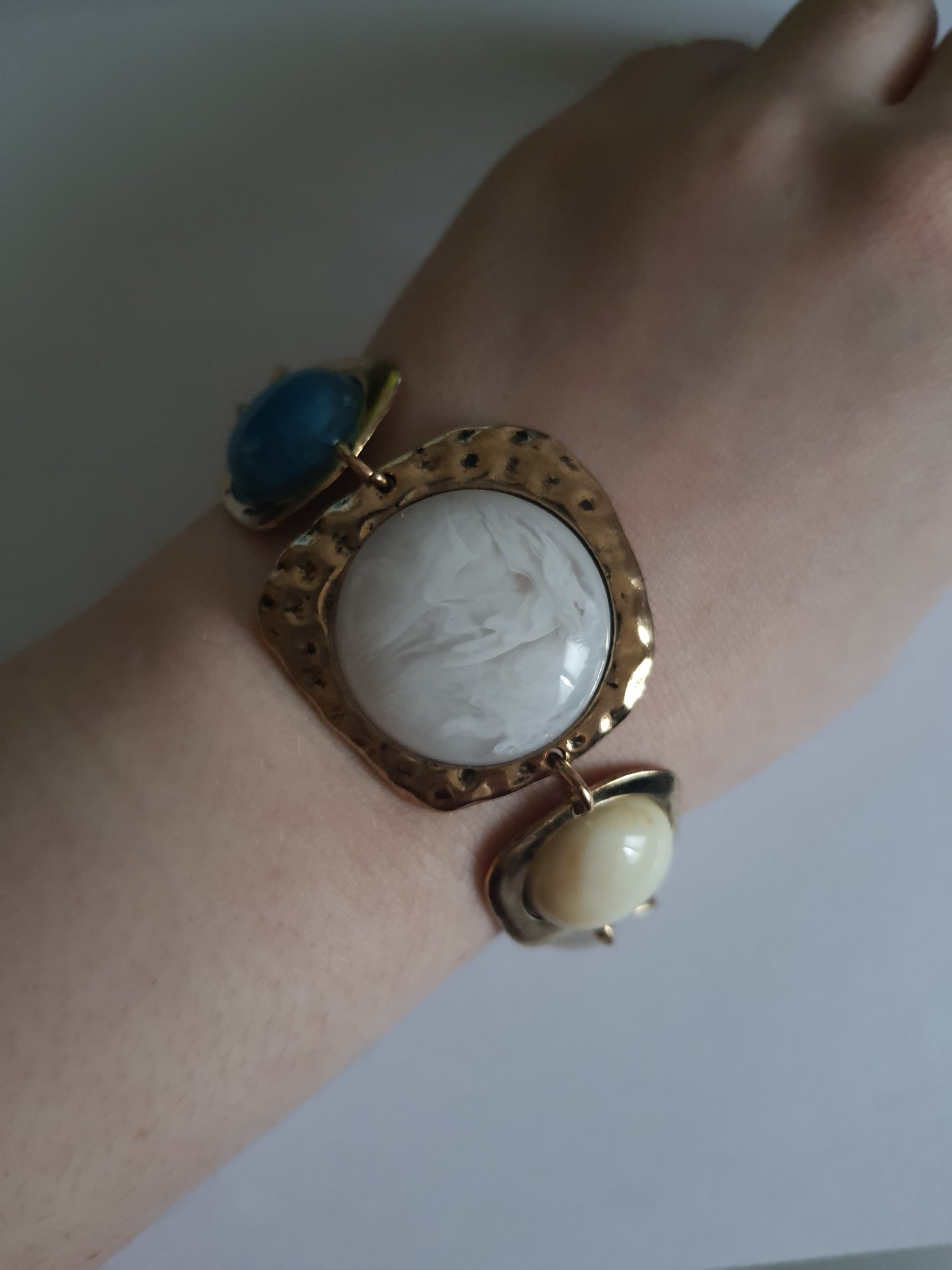 Artystyczna bransoletka damska z medalionami w kolorach marmuru, niebieskiego i brązu w nieregularnych złotych ramkach. Długość 20 cm. Styl boho, wyrazisty design. Stal nierdzewna, stal chirurgiczna. Rouge Bizu.

