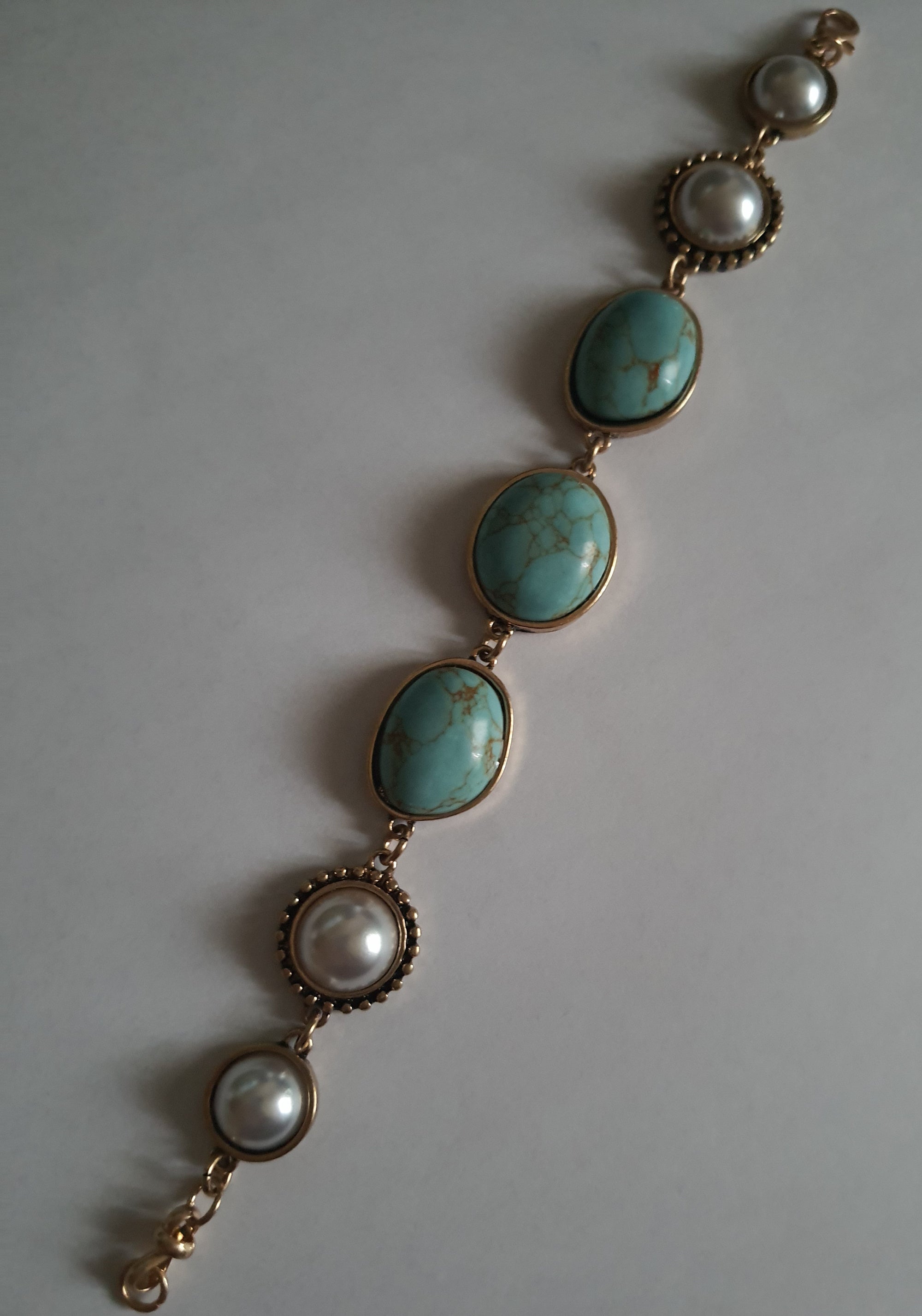 Bransoletka w stylu vintage ze złotą oprawą, ozdobiona turkusowymi kamieniami i perłami. Długość 20 cm. Klasyczna, elegancka forma. Biżuteria ze stali nierdzewnej. Rouge Bizu.

