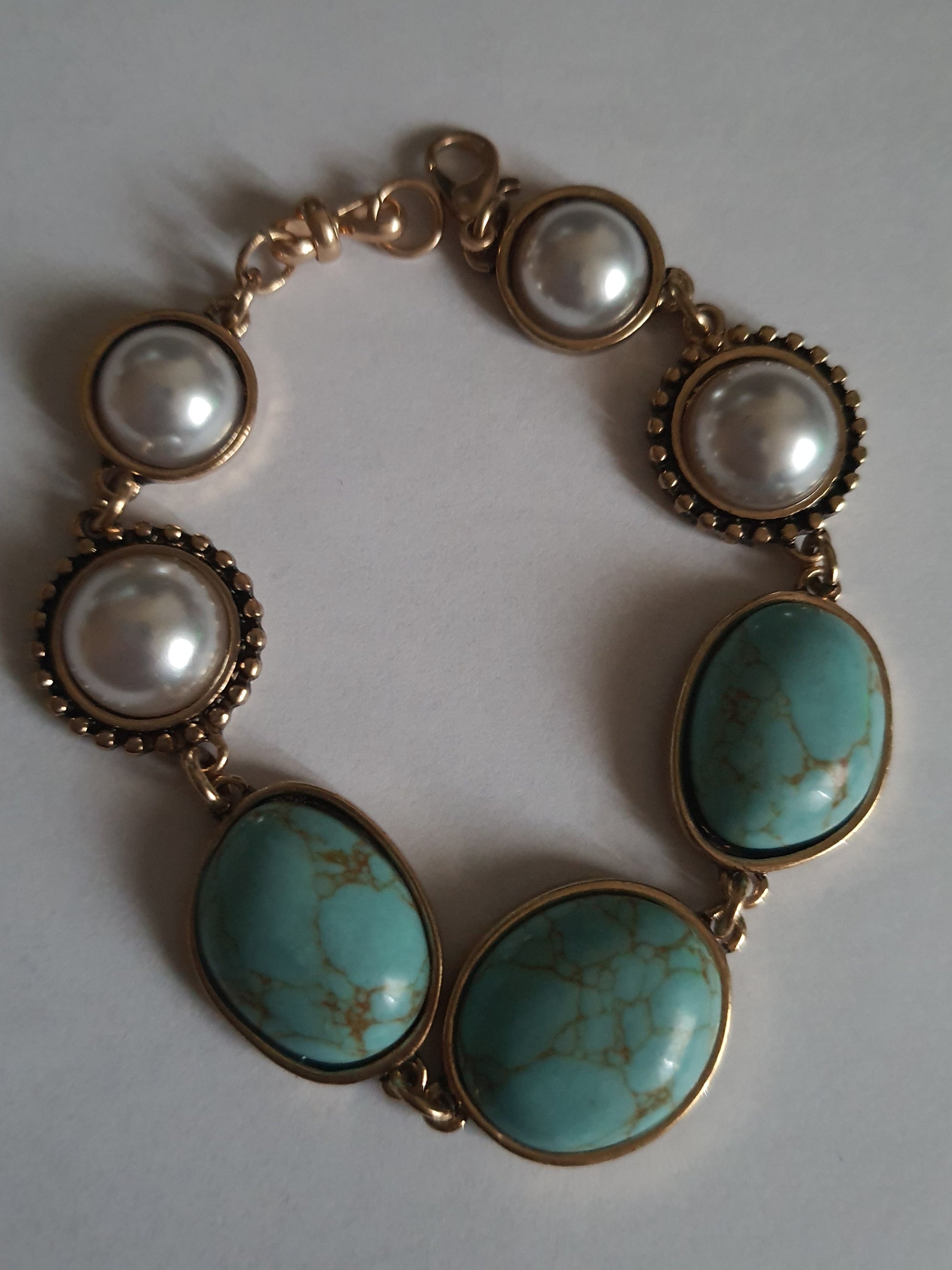 Bransoletka w stylu vintage ze złotą oprawą, ozdobiona turkusowymi kamieniami i perłami. Długość 20 cm. Klasyczna, elegancka forma. Biżuteria ze stali nierdzewnej. Rouge Bizu.

