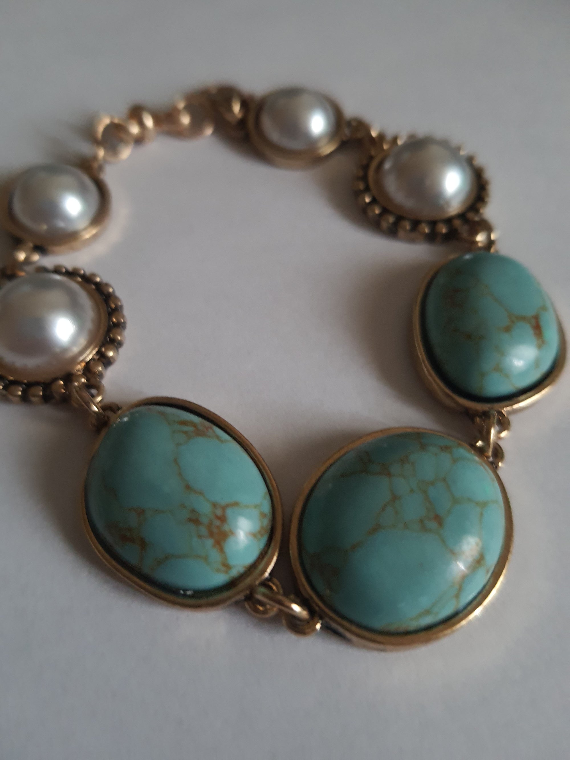 Bransoletka w stylu vintage ze złotą oprawą, ozdobiona turkusowymi kamieniami i perłami. Długość 20 cm. Klasyczna, elegancka forma. Biżuteria ze stali nierdzewnej. Rouge Bizu.

