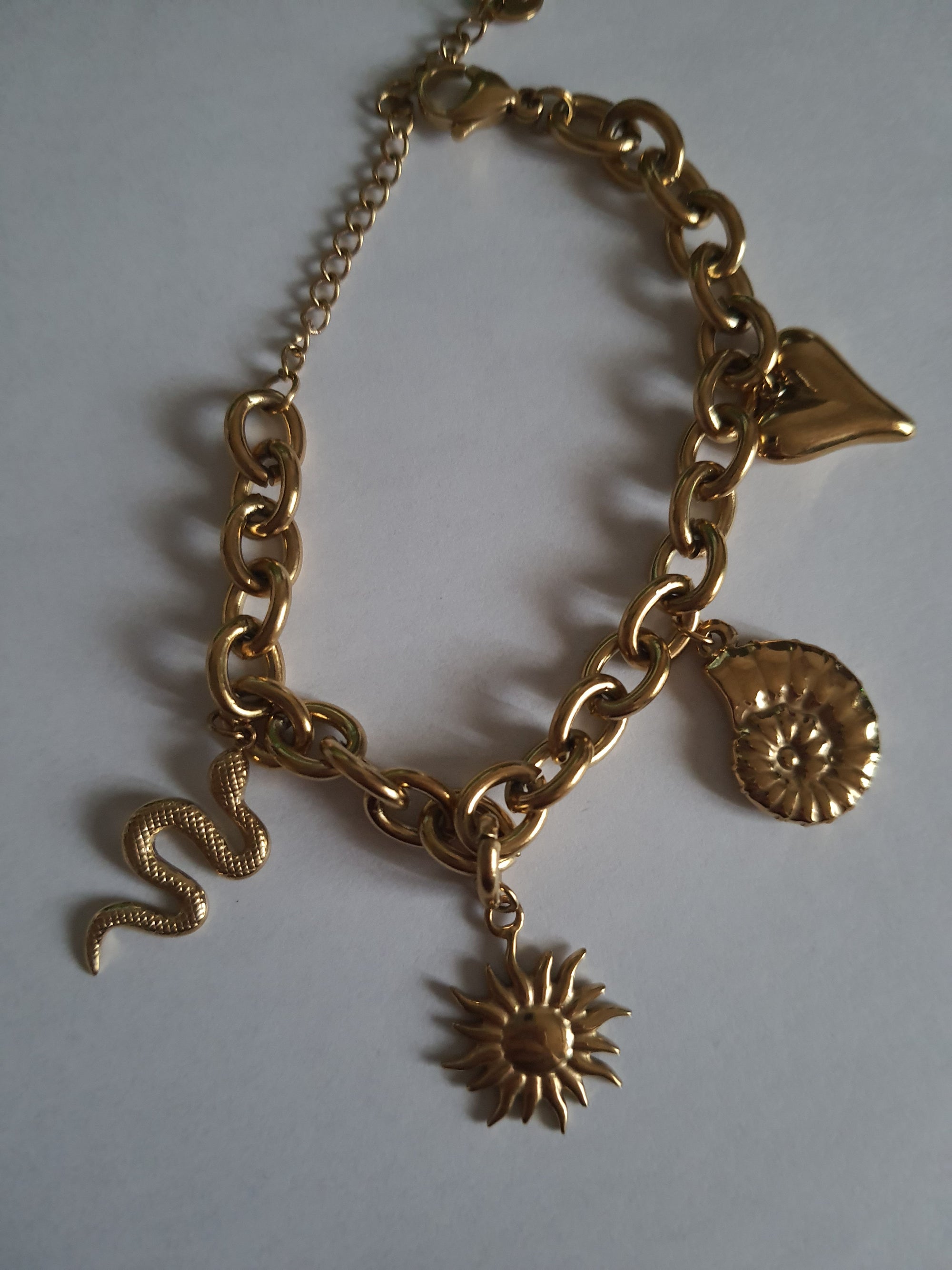 Złota bransoletka w stylu boho z zawieszkami: słońce, muszla, serce, wąż. Regulowana długość 25–30 cm. Talizmaniczna, ze stali nierdzewnej, stal chirurgiczna. Rouge Bizu.

