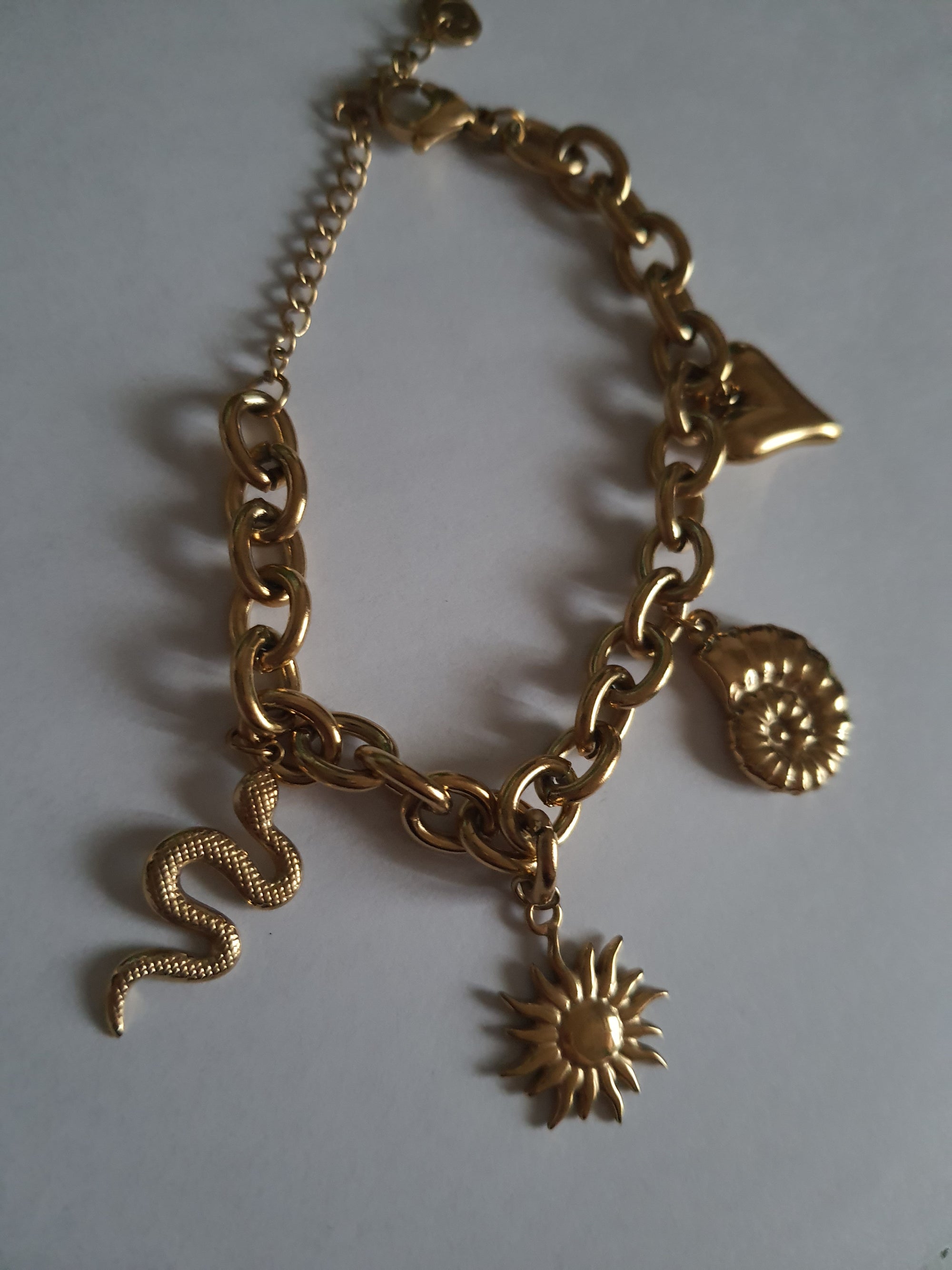 Złota bransoletka w stylu boho z zawieszkami: słońce, muszla, serce, wąż. Regulowana długość 25–30 cm. Talizmaniczna, ze stali nierdzewnej, stal chirurgiczna. Rouge Bizu.

