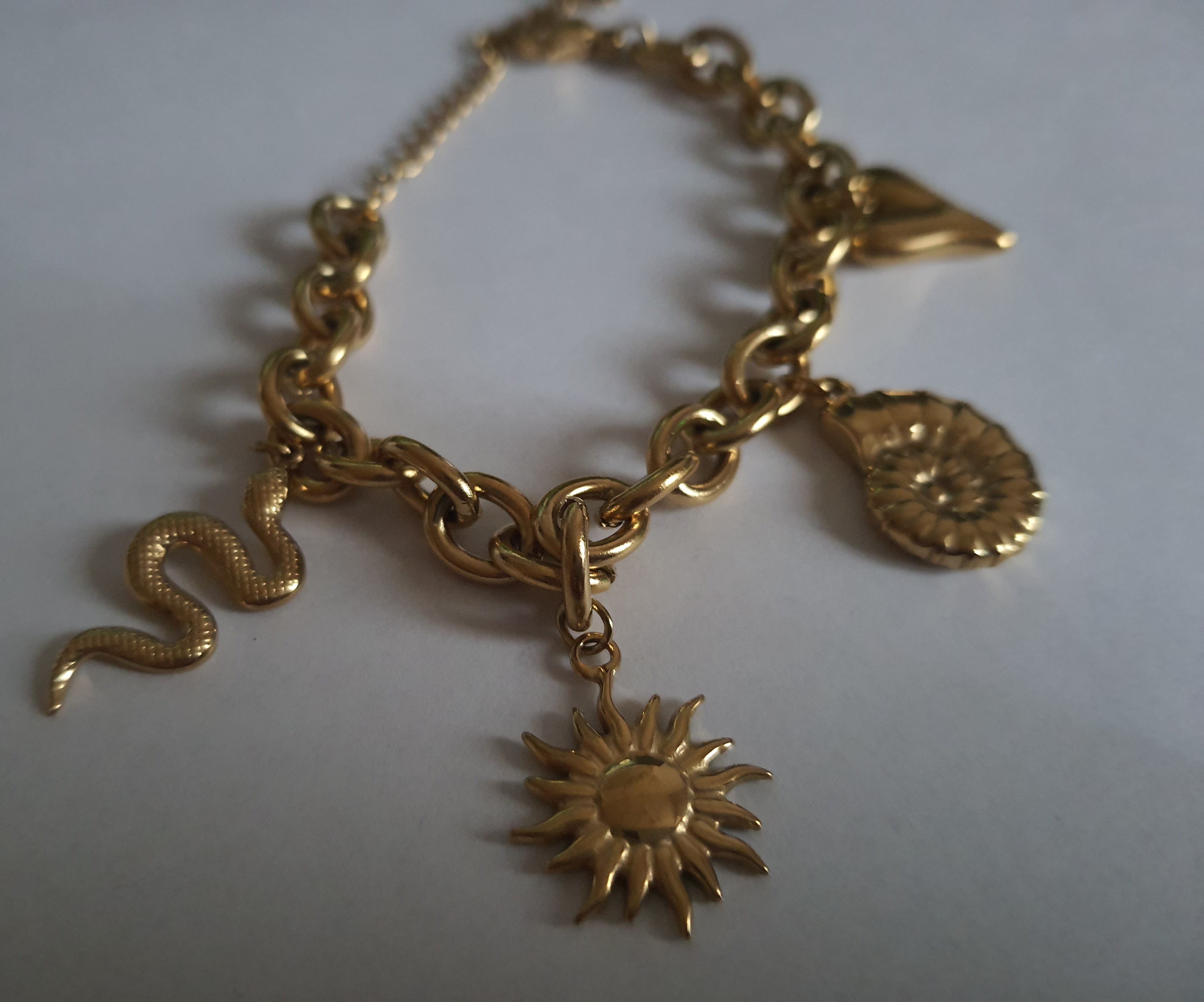 Złota bransoletka w stylu boho z zawieszkami: słońce, muszla, serce, wąż. Regulowana długość 25–30 cm. Talizmaniczna, ze stali nierdzewnej, stal chirurgiczna. Rouge Bizu.

