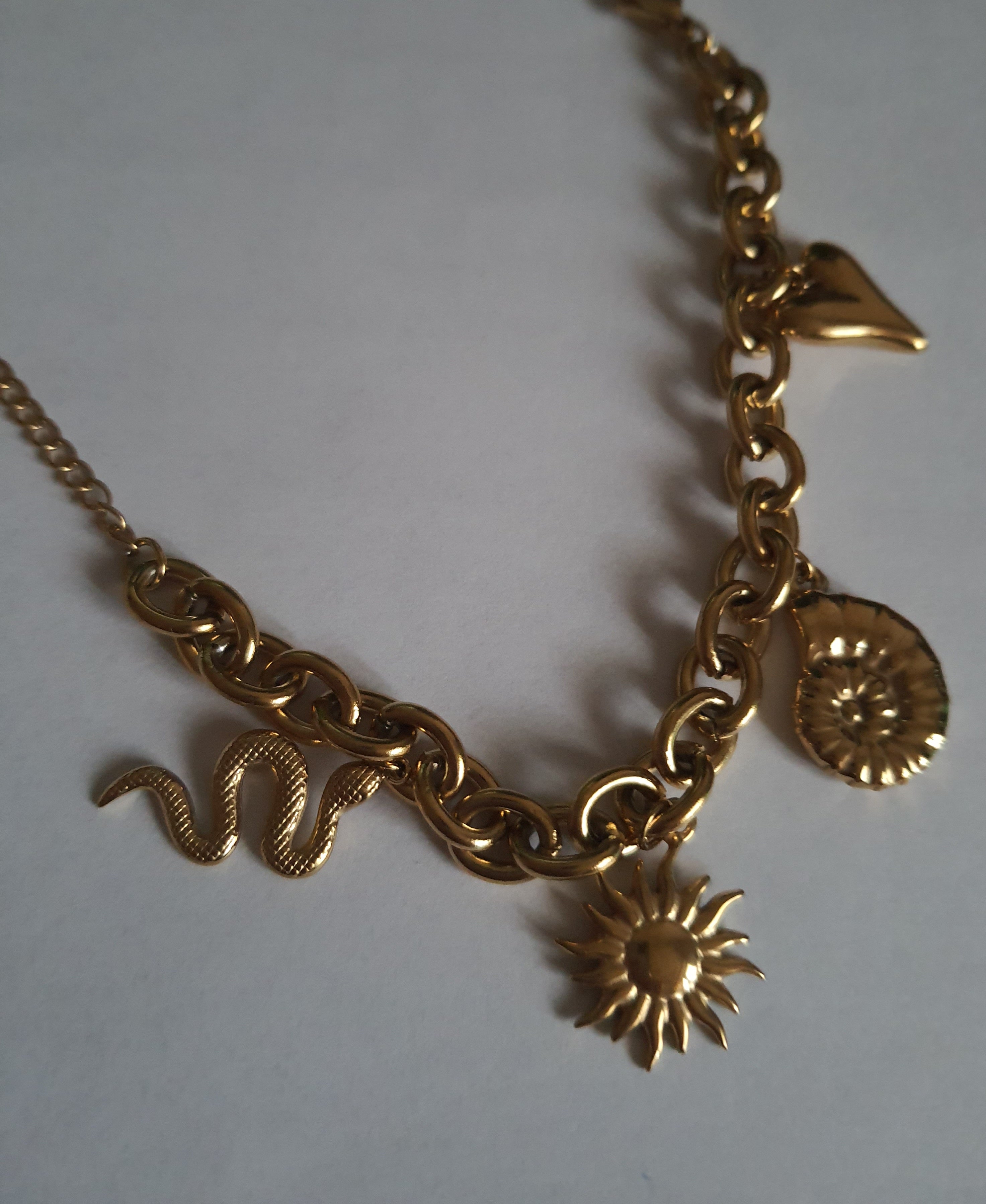 Złota bransoletka w stylu boho z zawieszkami: słońce, muszla, serce, wąż. Regulowana długość 25–30 cm. Talizmaniczna, ze stali nierdzewnej, stal chirurgiczna. Rouge Bizu.

