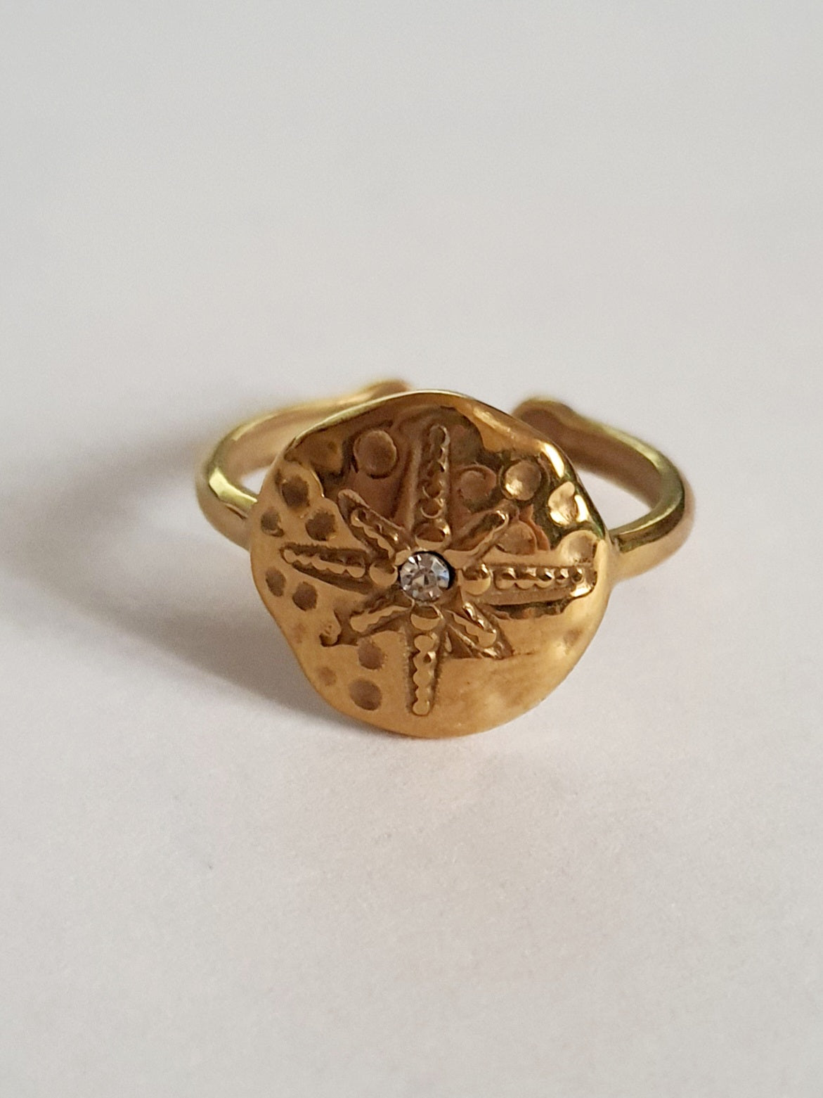 Złoty pierścionek regulowany, rozmiar 19 mm, z motywem tłoczonej gwiazdy morskiej i centralną cyrkonią. Styl boho i vintage, stal nierdzewna, stal chirurgiczna. Rouge Bizu.


