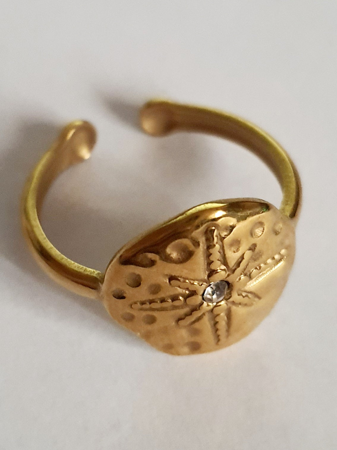 Złoty pierścionek regulowany, rozmiar 19 mm, z motywem tłoczonej gwiazdy morskiej i centralną cyrkonią. Styl boho i vintage, stal nierdzewna, stal chirurgiczna. Rouge Bizu.

