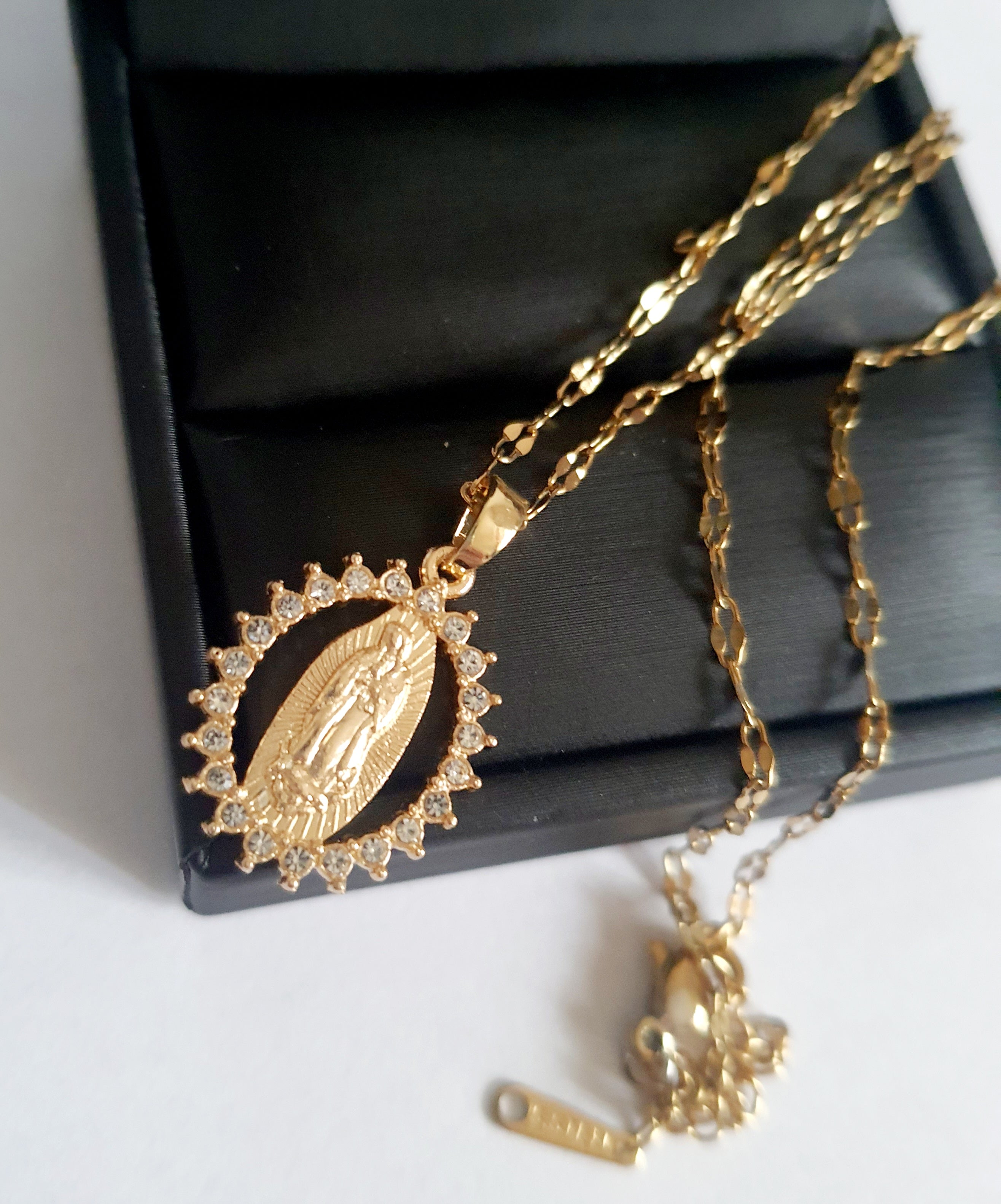 Złoty łańcuszek o długości 40–46 cm z wisiorkiem Matki Boskiej otoczonym cyrkoniami. Styl sakralny, elegancki. Stal nierdzewna, Rouge Bizu.

