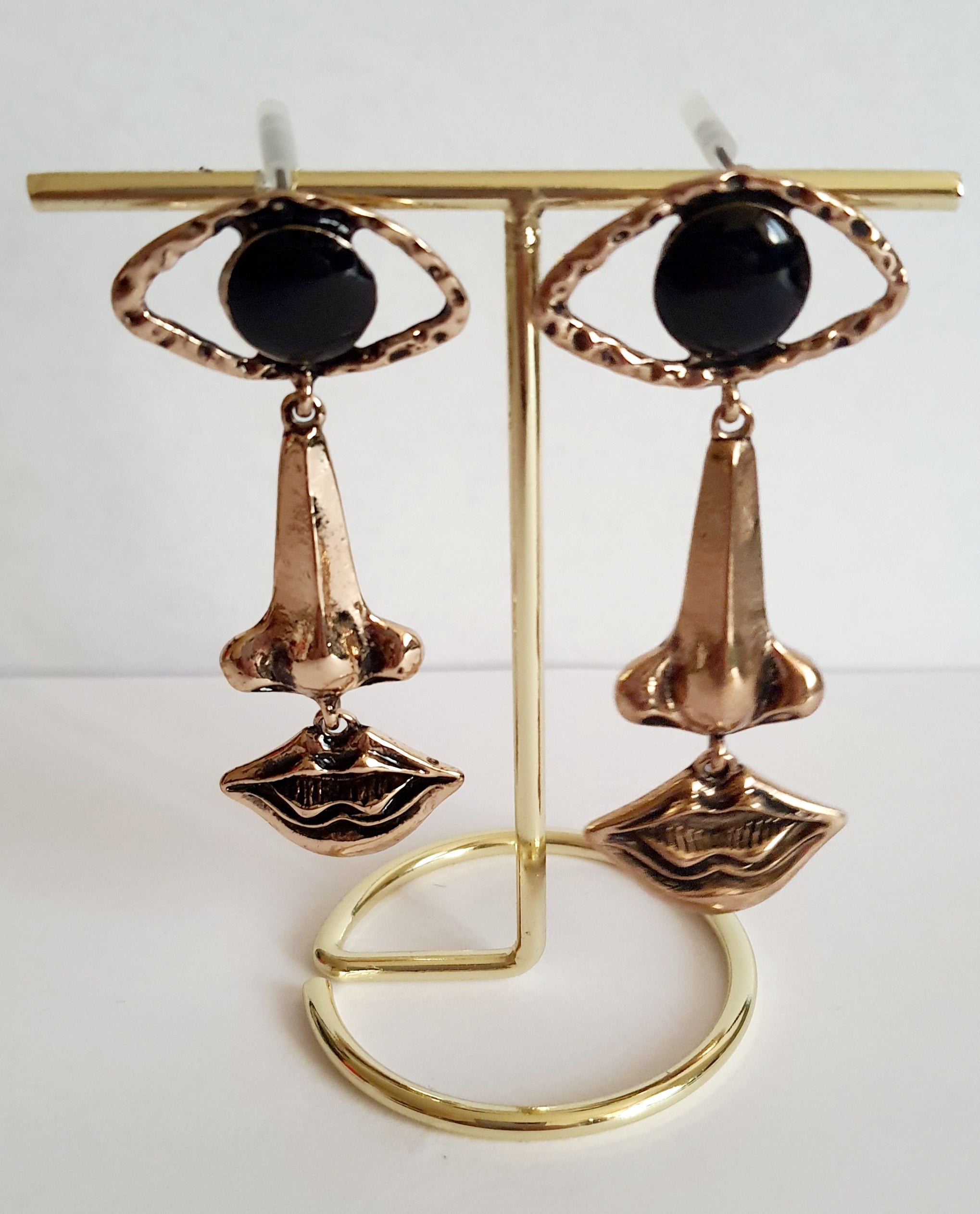 Wiszące kolczyki 7 cm ze stali nierdzewnej w kolorze złotym w kształcie oka, nosa i ust, z czarnym kamieniem w centrum oka. Rouge Bizu, stal nierdzewna, stal chirurgiczna.

