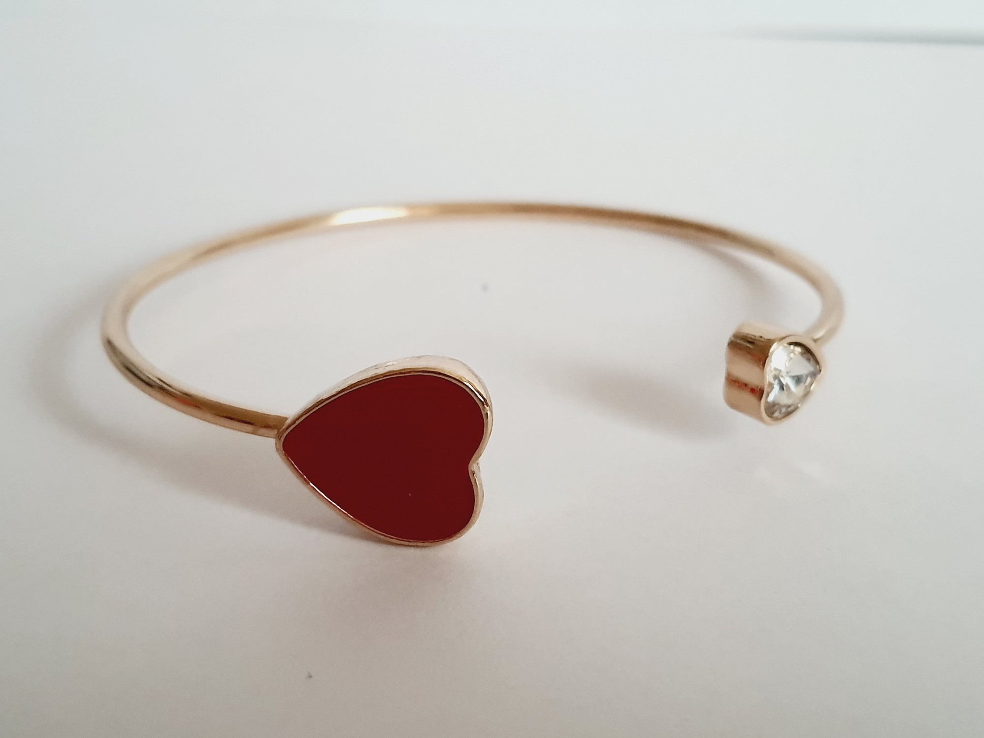 Sztywna złota bransoletka ze stali nierdzewnej z czerwonym sercem i bezbarwnym kryształem, minimalistyczny design. Rouge Bizu.

