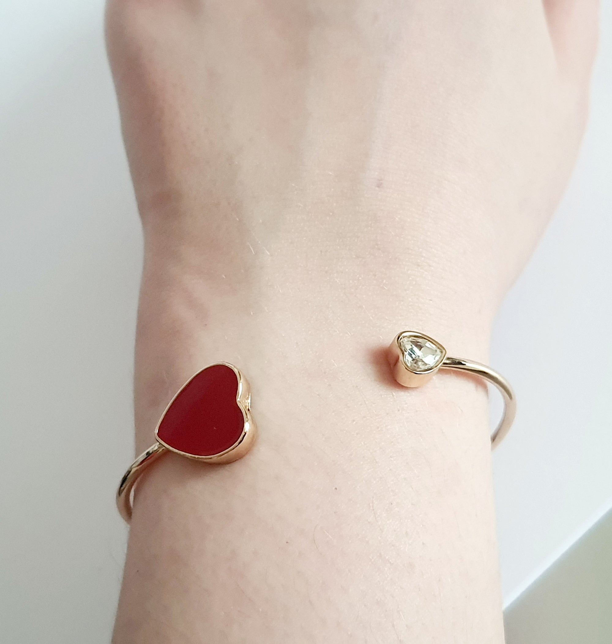 Sztywna złota bransoletka ze stali nierdzewnej z czerwonym sercem i bezbarwnym kryształem, minimalistyczny design. Rouge Bizu.


