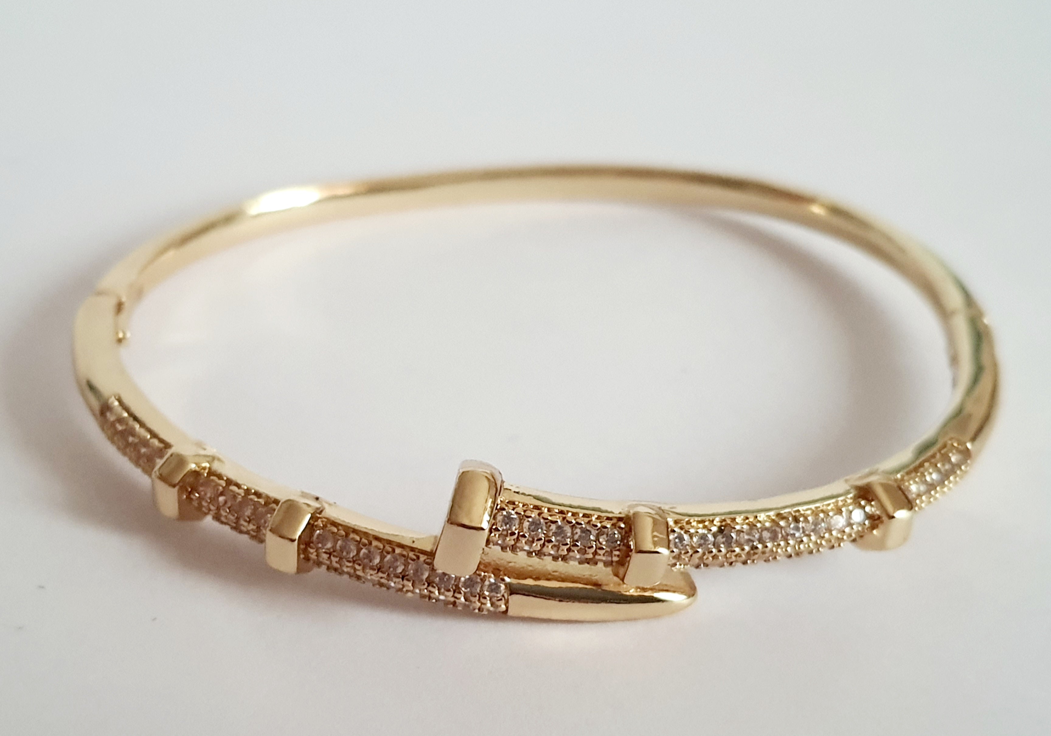 Złota bransoletka sztywna o średnicy 6 cm, zdobiona białymi cyrkoniami, nowoczesny elegancki design, stal nierdzewna. Rouge Bizu.

