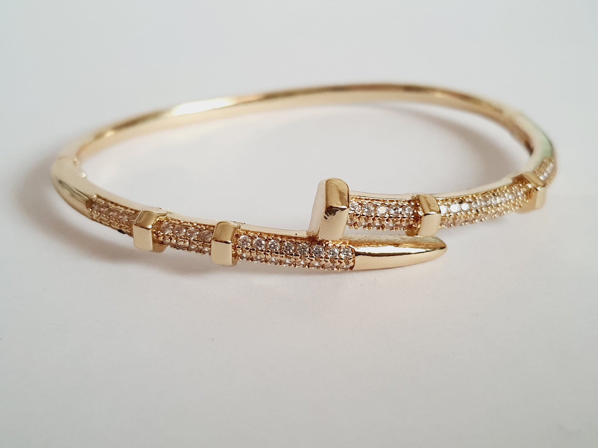 Złota bransoletka sztywna o średnicy 6 cm, zdobiona białymi cyrkoniami, nowoczesny elegancki design, stal nierdzewna. Rouge Bizu.

