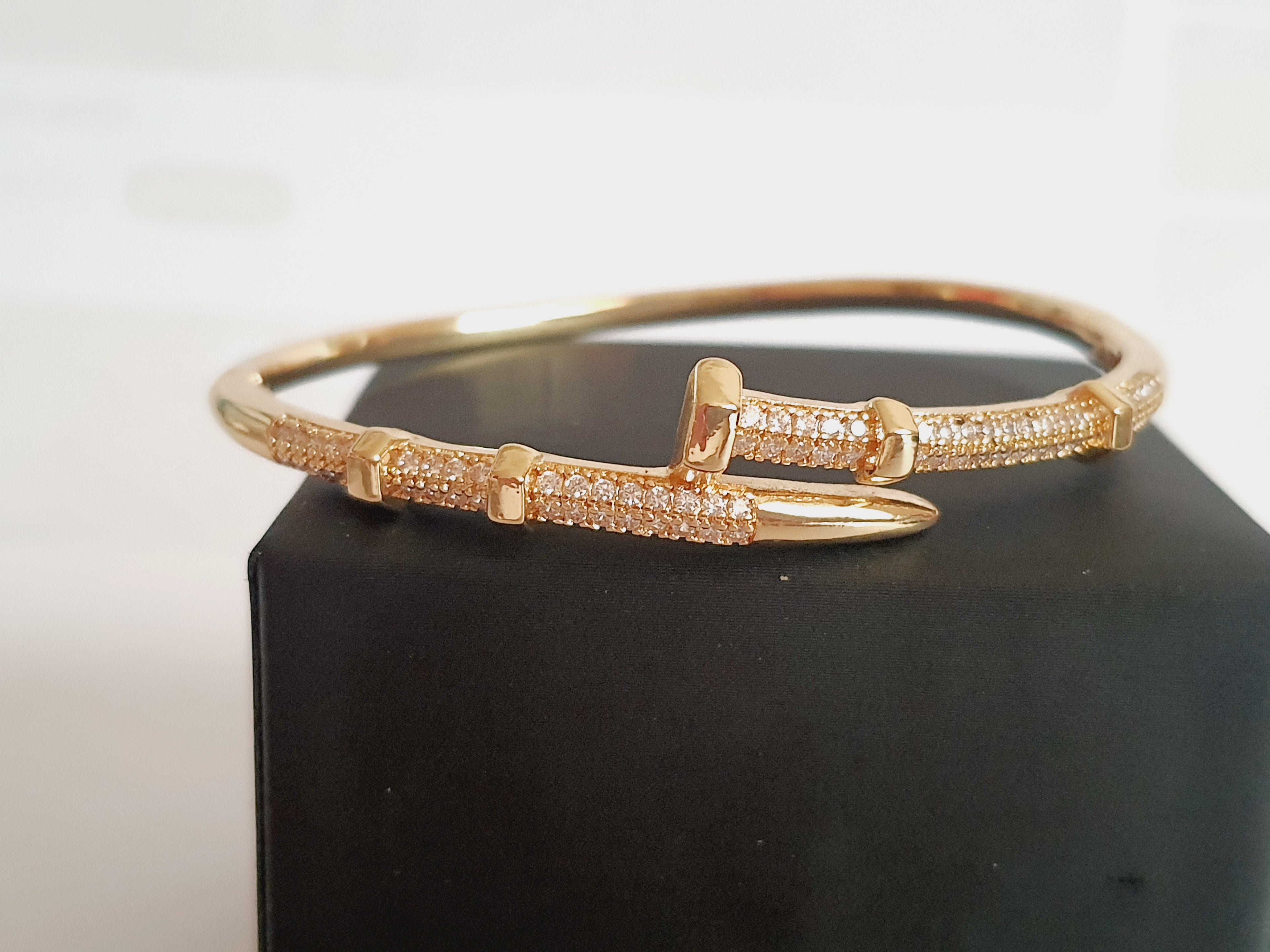 Złota bransoletka sztywna o średnicy 6 cm, zdobiona białymi cyrkoniami, nowoczesny elegancki design, stal nierdzewna. Rouge Bizu.

