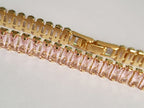 Bransoletka tenisowa ze stali nierdzewnej w złotej oprawie, zdobiona pudrowo-różowymi cyrkoniami, długość 19 cm. Klasyczna elegancja i romantyczny blask. Rouge Bizu.

